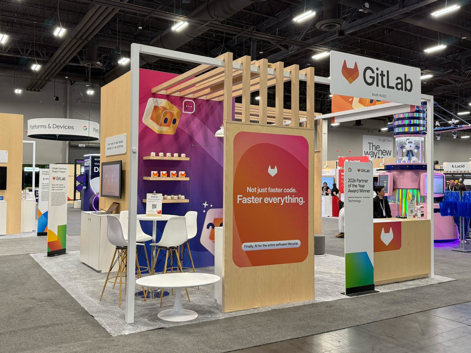 Colourful geometric GitLab Duo AI agent characters featured on a large exhibition booth display, bringing the brand's playful illustration system to life at an event.