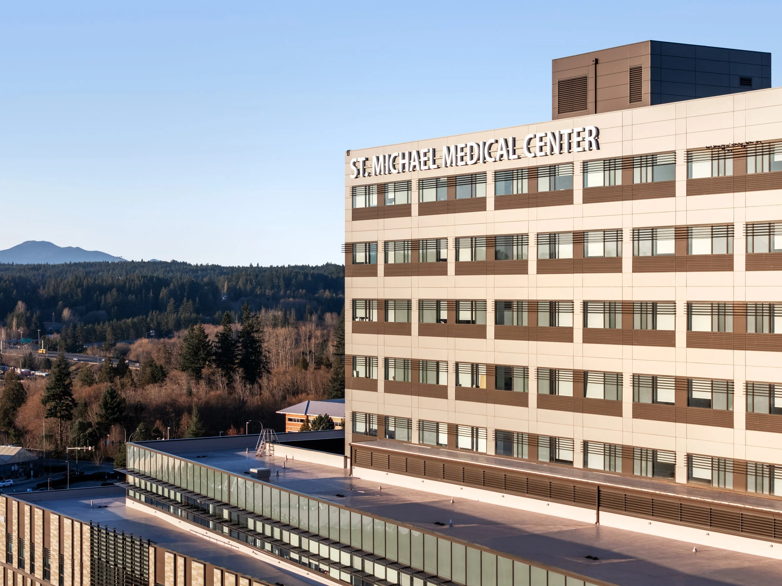 Exterior view of St. Michael Medical Center building with a mountain in the background, blue sky, and surrounding trees.