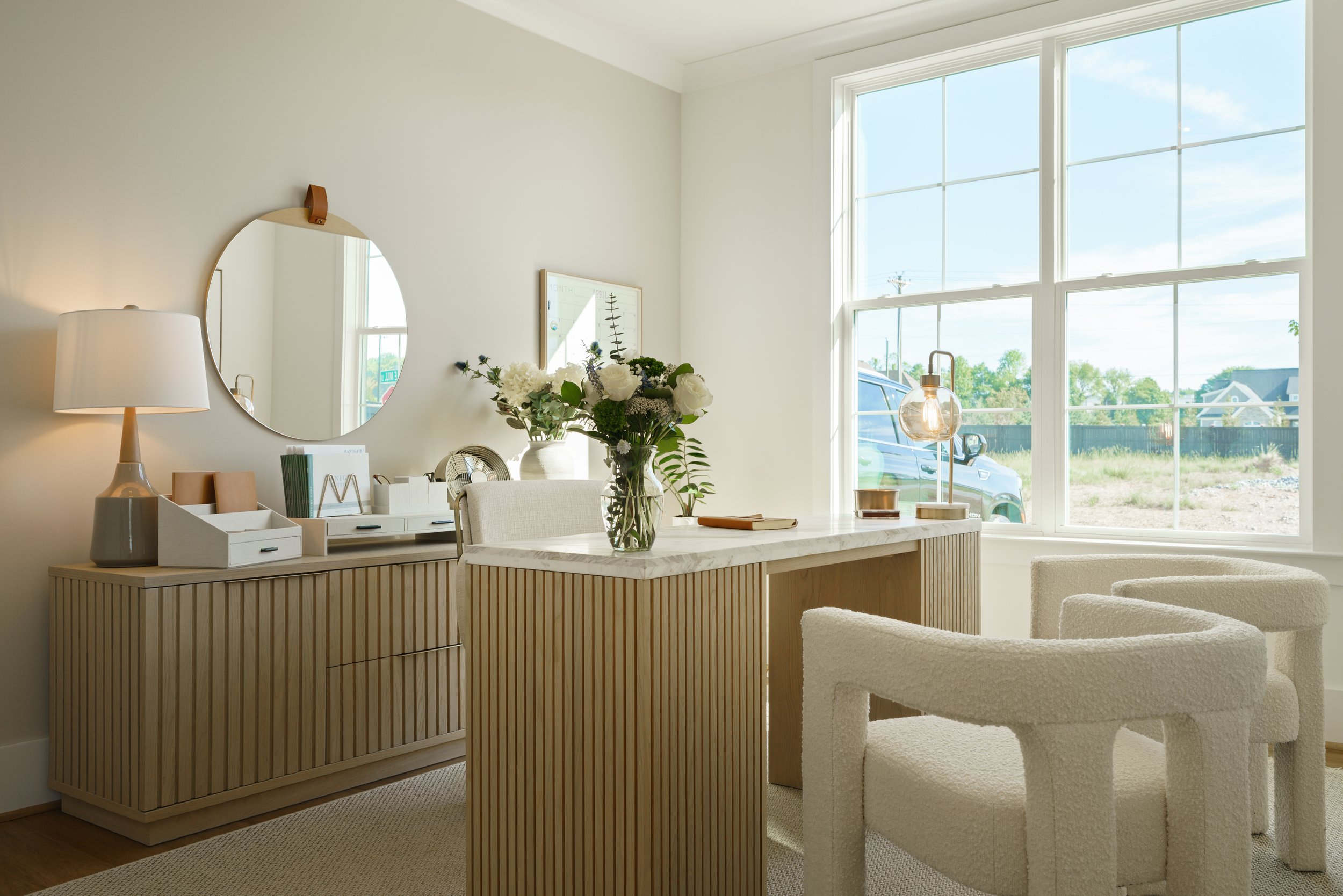 A bright, modern living room with large windows, a marble-topped table with a plant, and a fluffy cream-colored armchair.