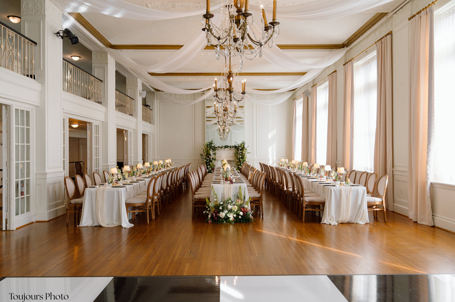 Elegant banquet hall decorated for a wedding reception with long tables, floral arrangements, and chandeliers.