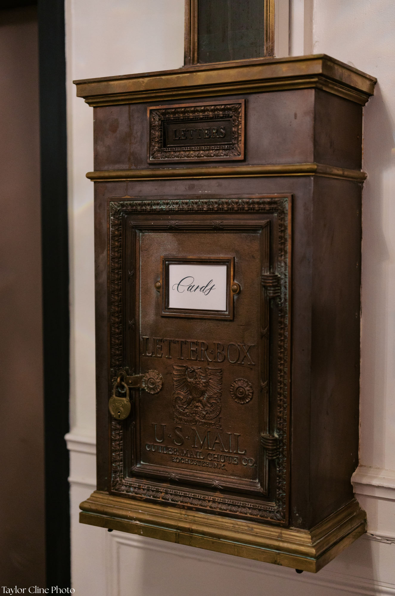 A vintage copper letterbox with ornate detailing, engraved with the words 'Letterbox' and 'U.S. Mail', locks on the front, and a white sign with the word 'Cards' on the door.