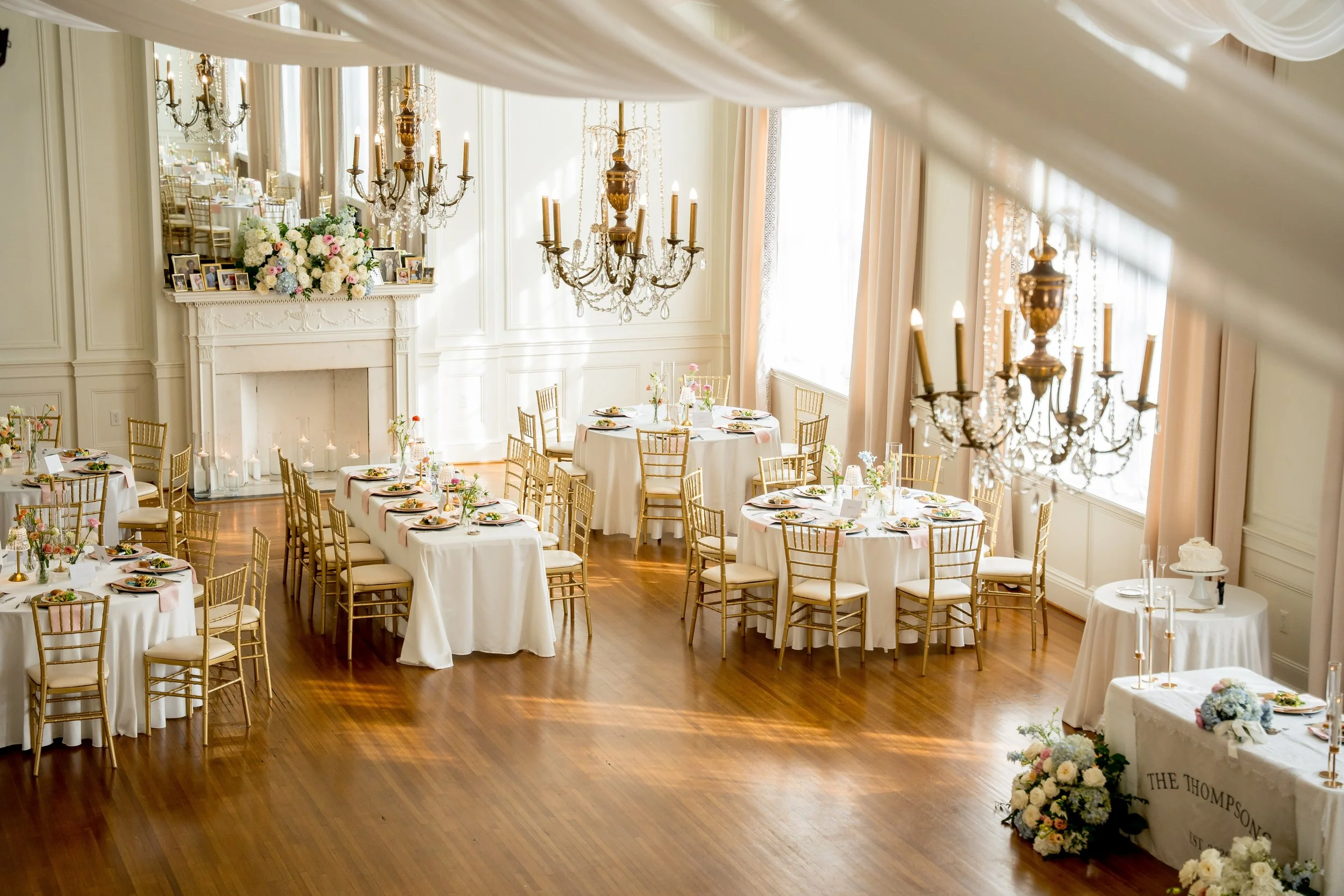 Elegant event space decorated with chandeliers, floral arrangements, and tables set for a celebration.