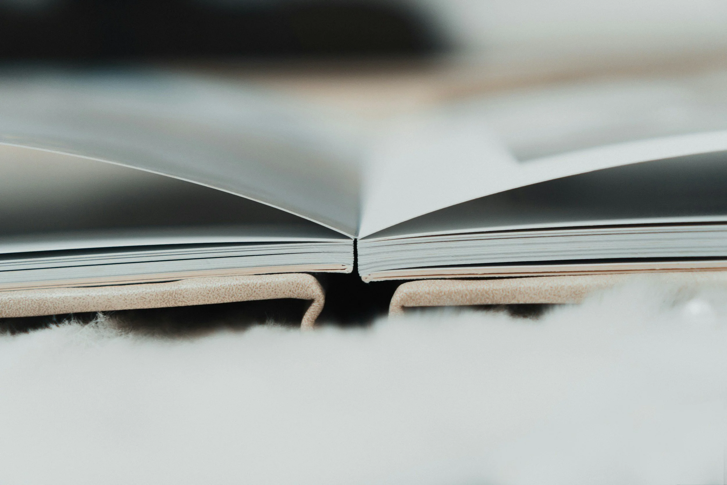 Close-up of an open book with a white cover and beige binding, laid flat on a white surface with a slightly fuzzy texture.