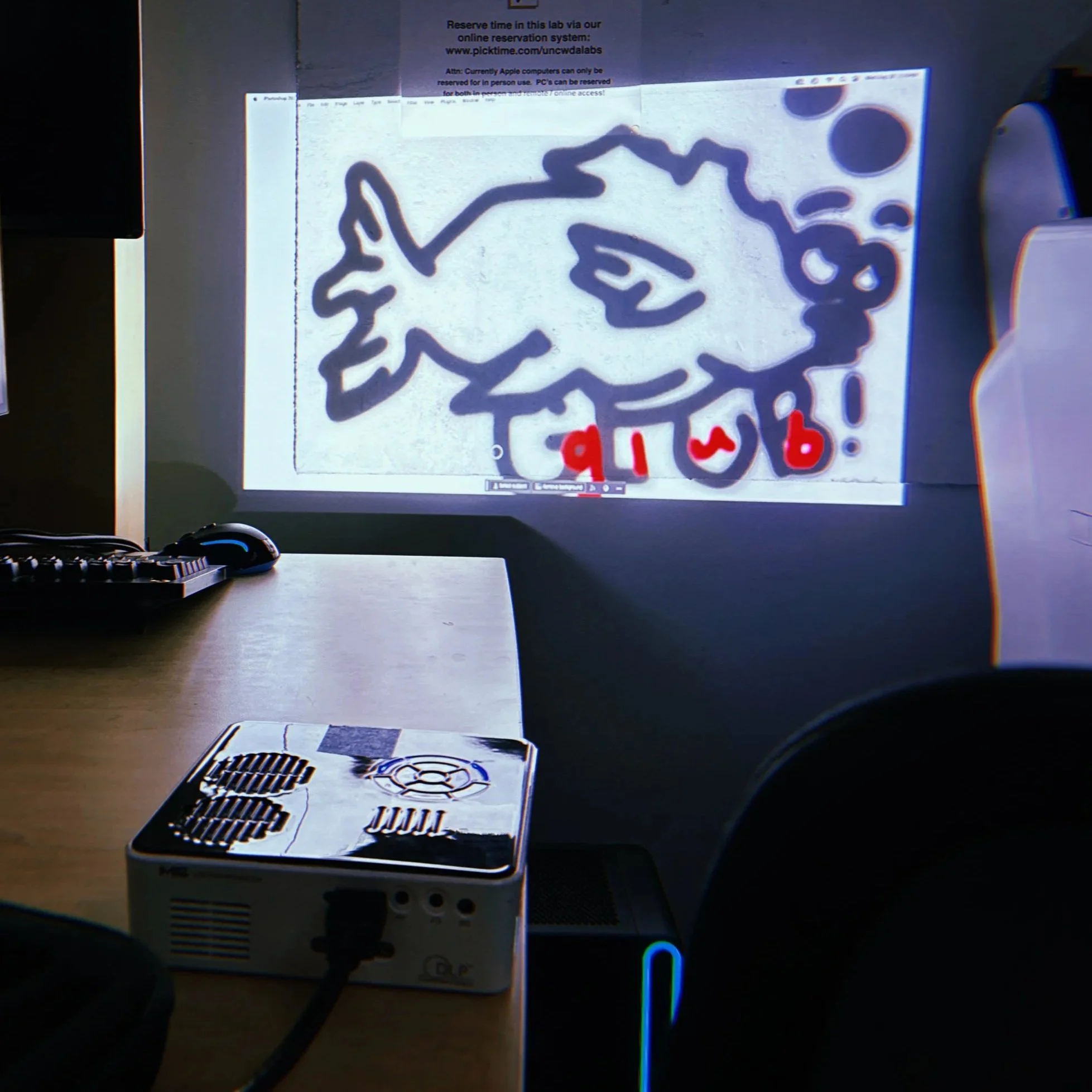 Photo of a computer screen displaying a logo with a star and a swirl, along with some red text at the bottom. There are electronic devices, including a keyboard and a desktop computer, visible on the desk in front of the screen.