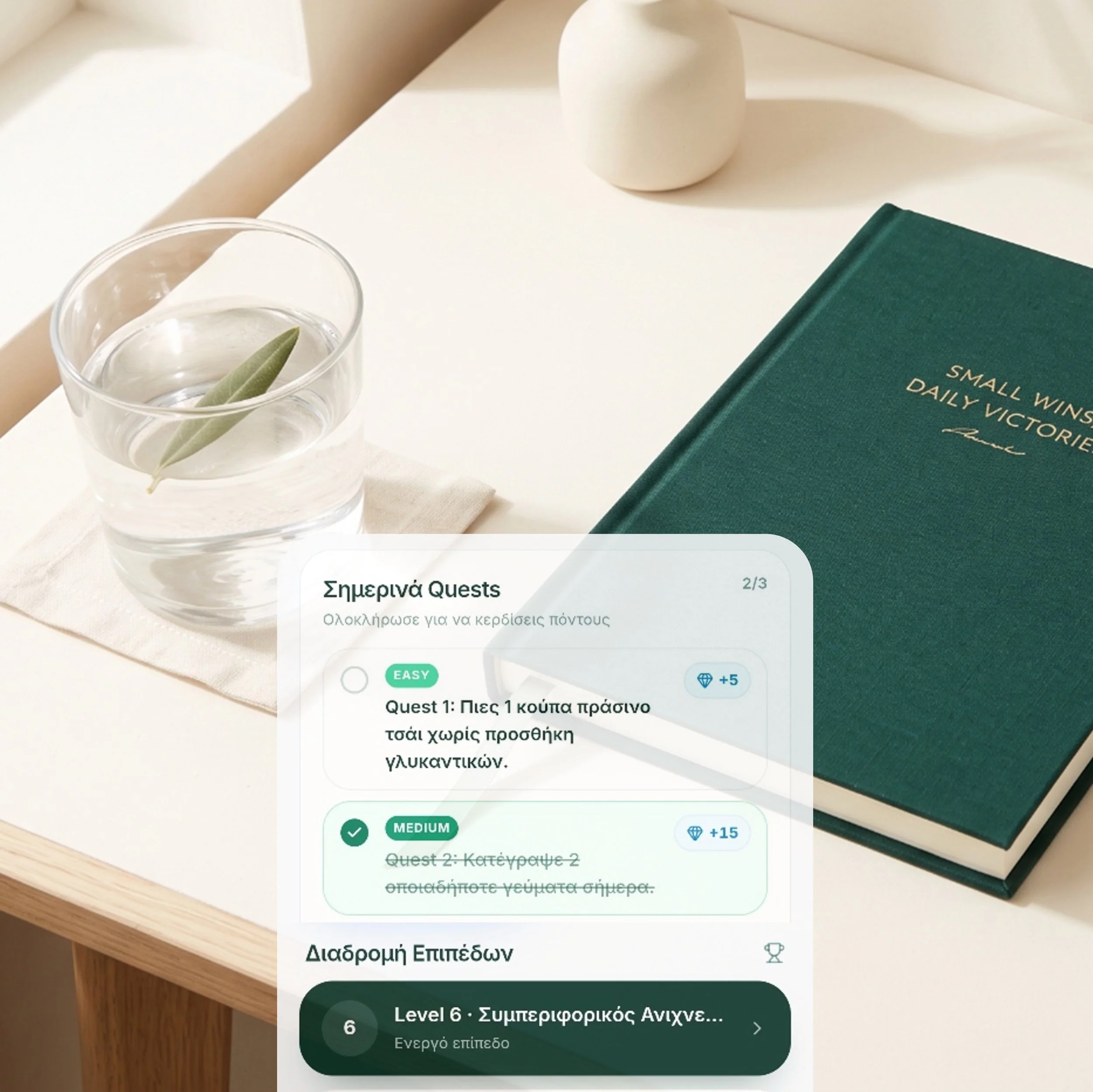 A close-up view of a table with a clear glass of water, a white decorative object resembling an elongated egg, a dark green book titled 'Small Wins Daily Victories', and a screen displaying a Greek language quiz or game interface with various levels and questions.