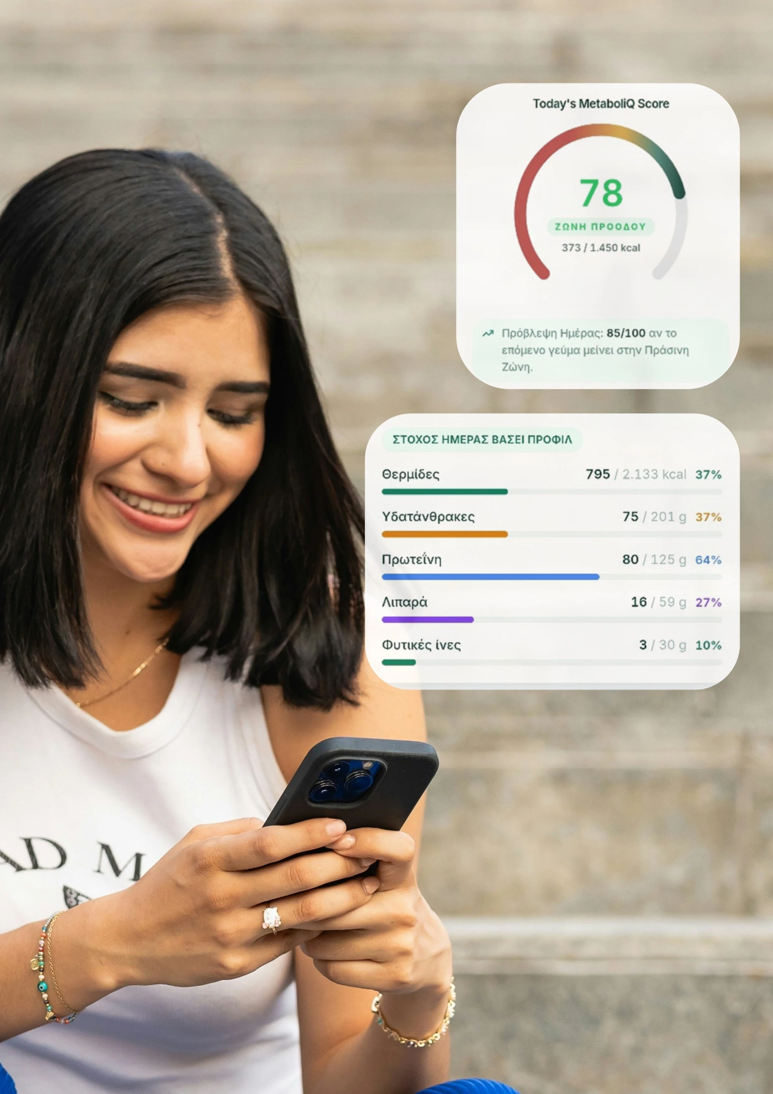 A smiling woman with dark hair, wearing a white t-shirt and jewelry, looking at her smartphone with a digital health monitoring app on the screen.