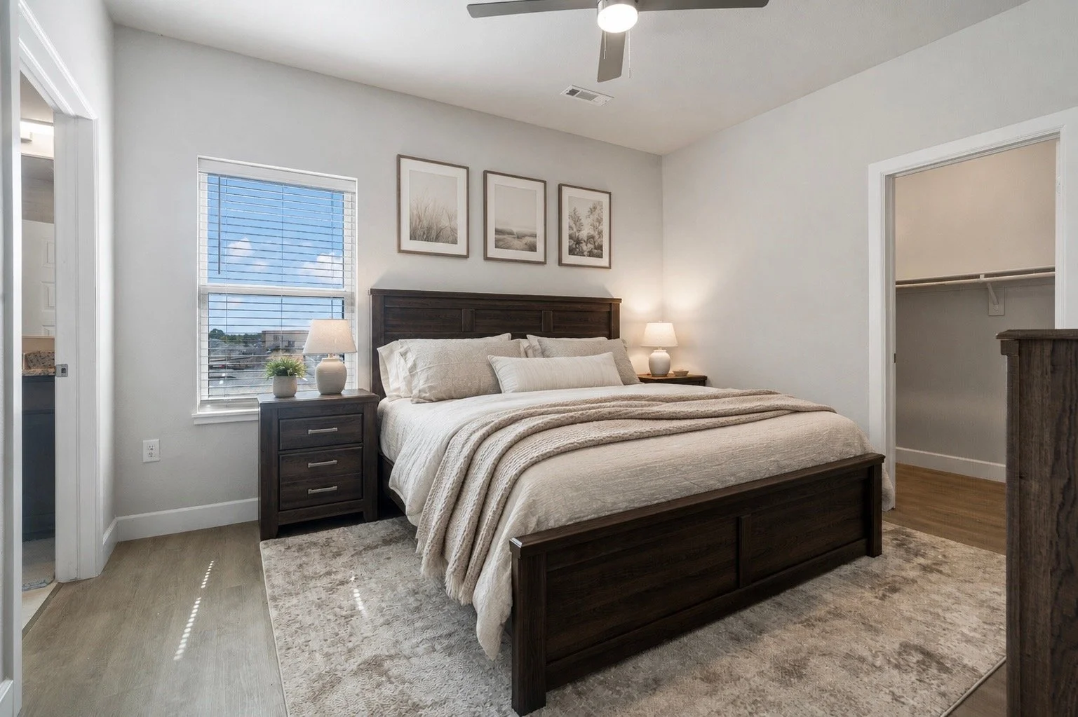 Bedroom with a dark wood bed, white bedding, two nightstands with lamps, three framed pictures above the bed, window with blinds, and open closet door.
