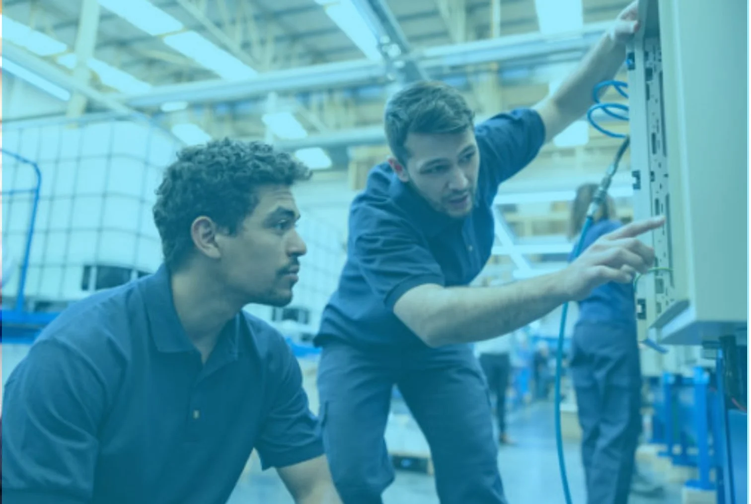 Two young men working on electrical equipment in a warehouse or industrial setting.