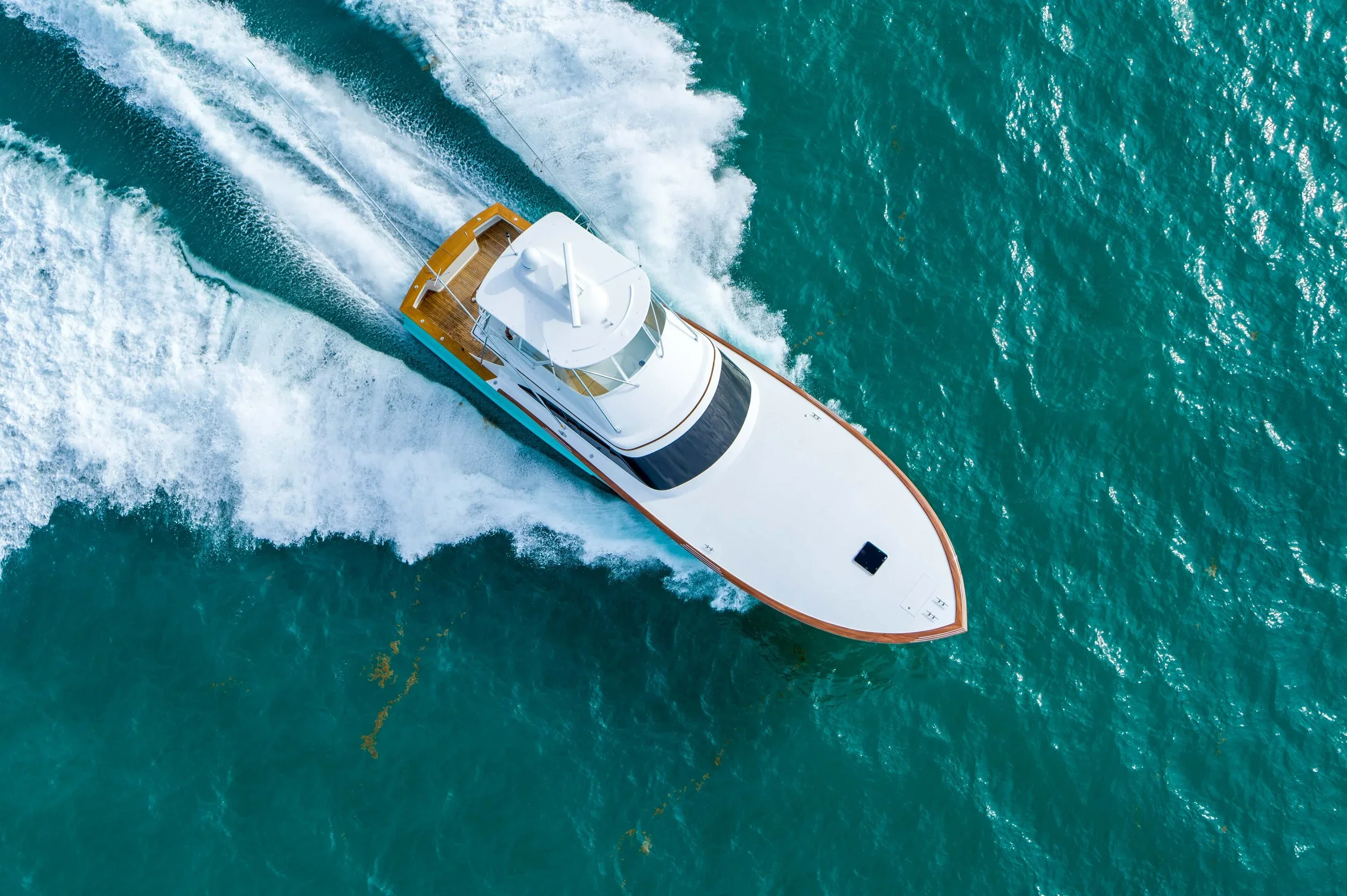 An aerial view of a white motor yacht sailing through the turquoise ocean, creating white wake behind it.