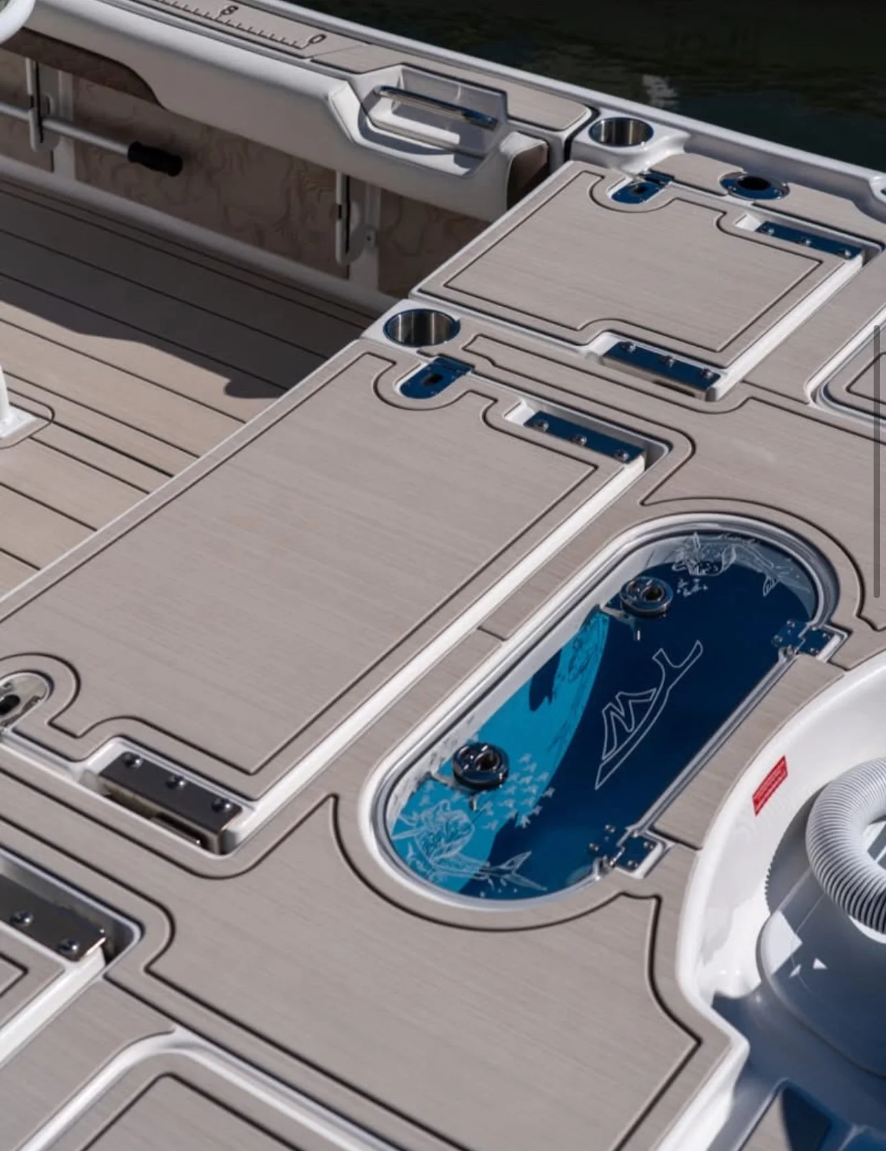 Close-up of a boat deck with built-in storage compartments, a small water feature with water design, and a gray hose on the right side.