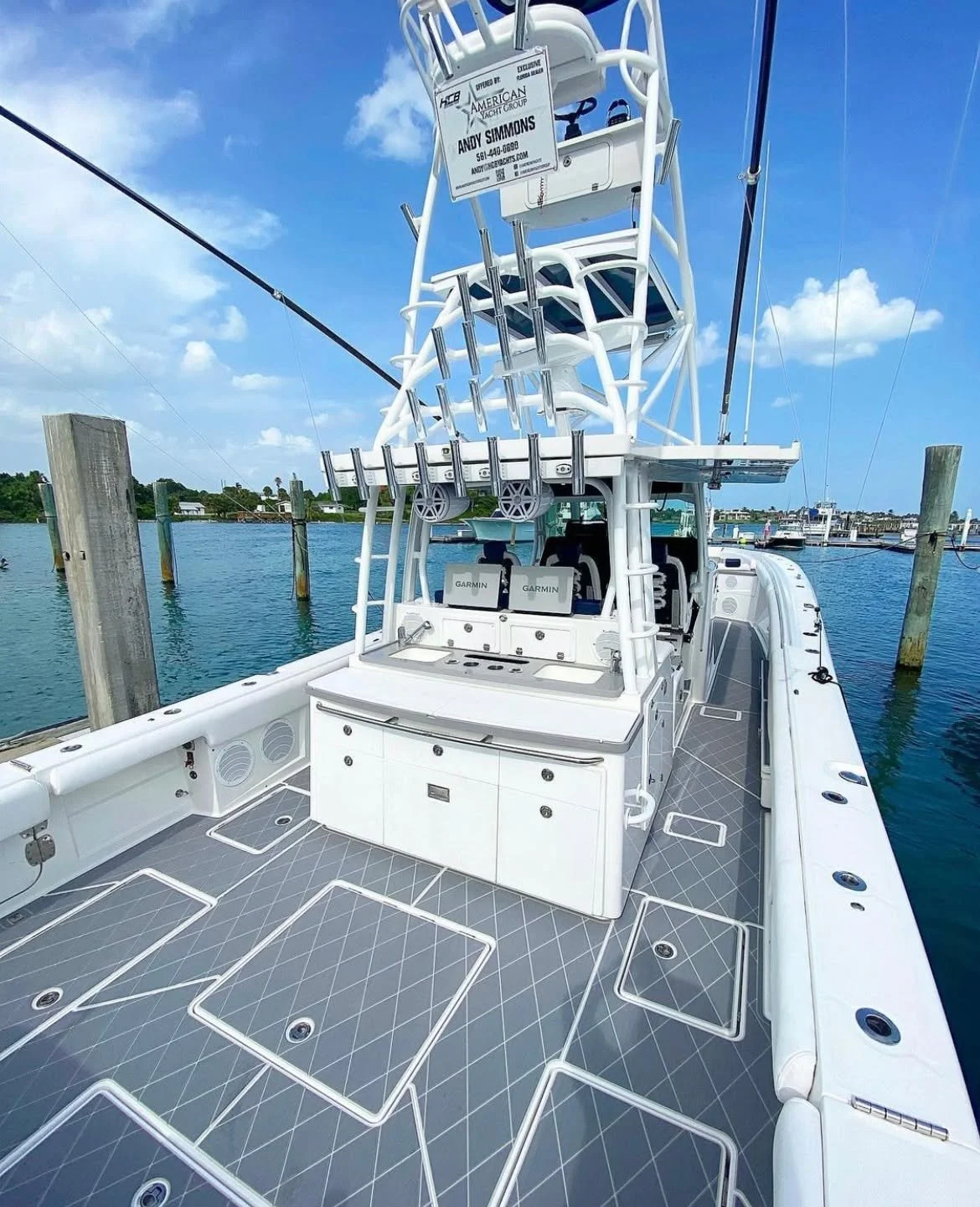 A white fishing boat docked at a marina with a tower of stacked chairs on top, a sign with contact info, and a gray deck with hatch covers.