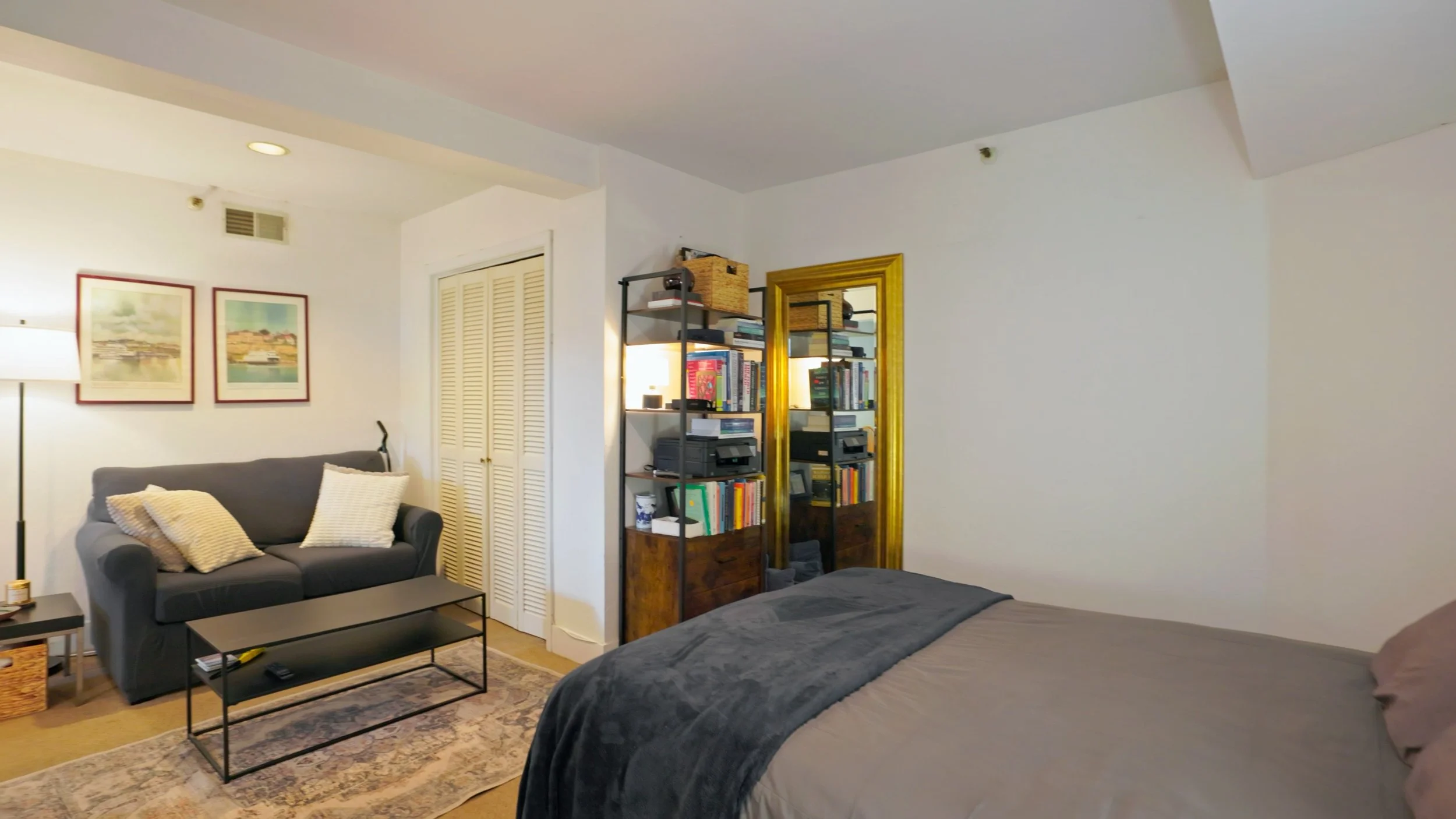 The living and sleeping area of the Garden Studio with a bed, bookcase, loveseat and coffee table.