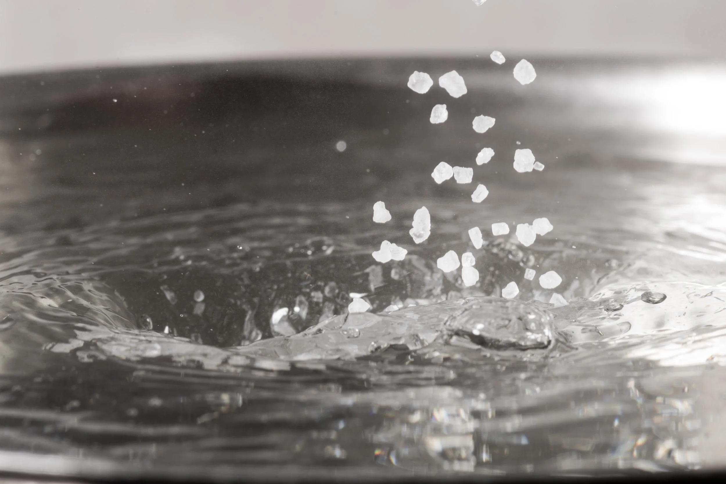 Close up of crystals being poured into a vat of clear water