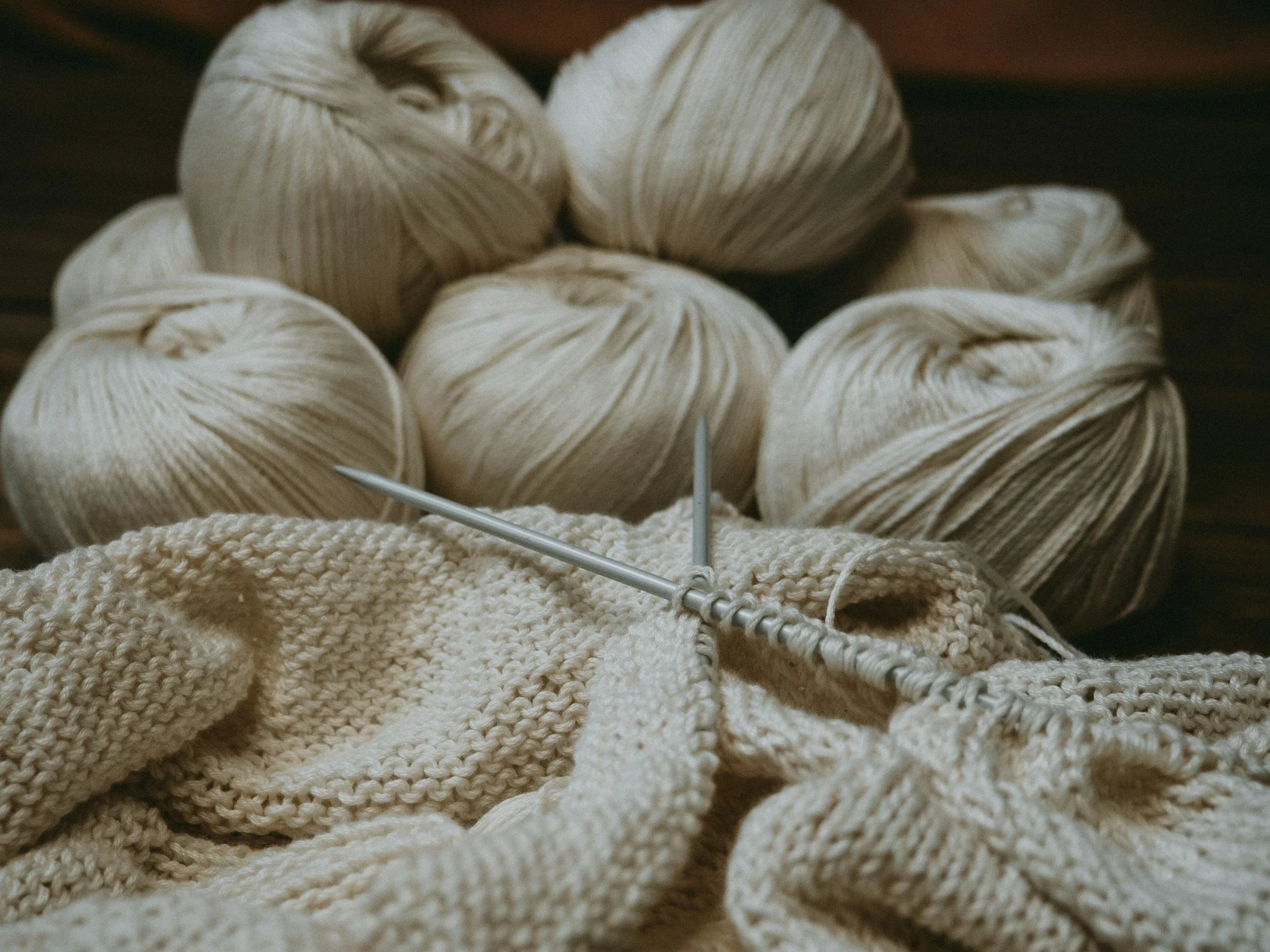 Strickwaren und Wollknäuel in neutralen Farben auf einem dunklen Hintergrund.