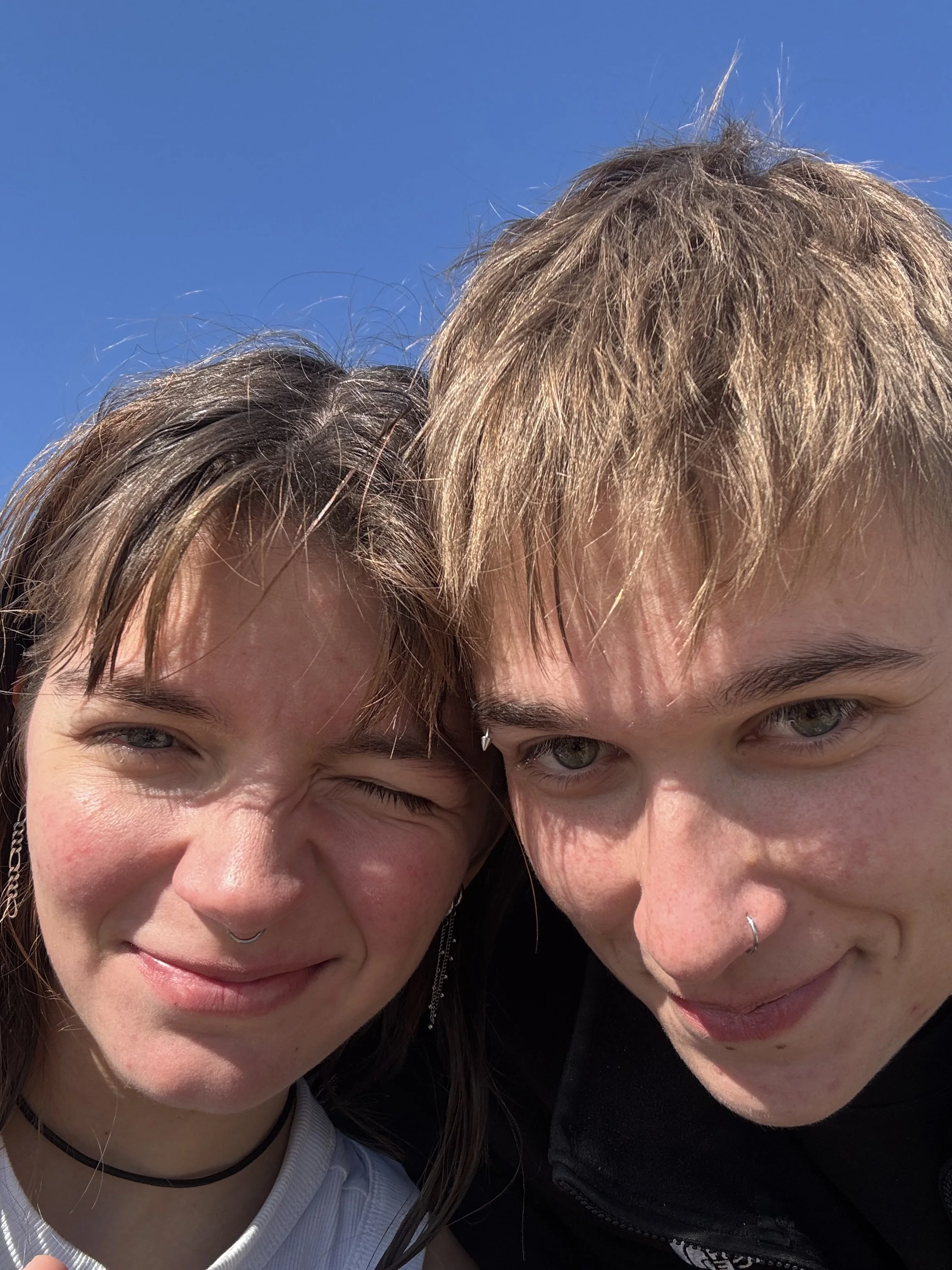 Nahaufnahme von zwei Menschen, die zusammen lachen unter einem klaren blauen Himmel.