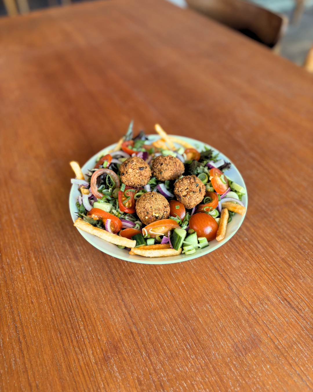 Falafelbowl med falafel, cherrytomater, agurk, forårsløg, peberfrugt, rødløg og sprøde pommes frites.