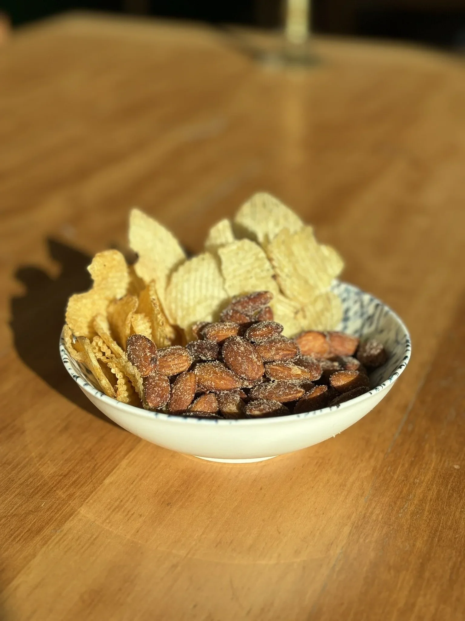 En skål med en blanding af chips, peanuts og mandler placeret på et træbord.