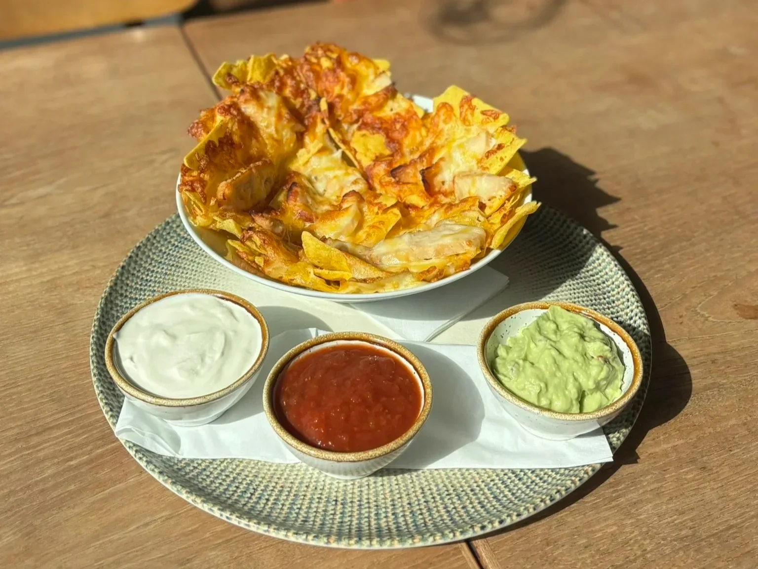 En tallerken med nachos med ost, tre små skåle med salsa, creme fraiche og guacamole.