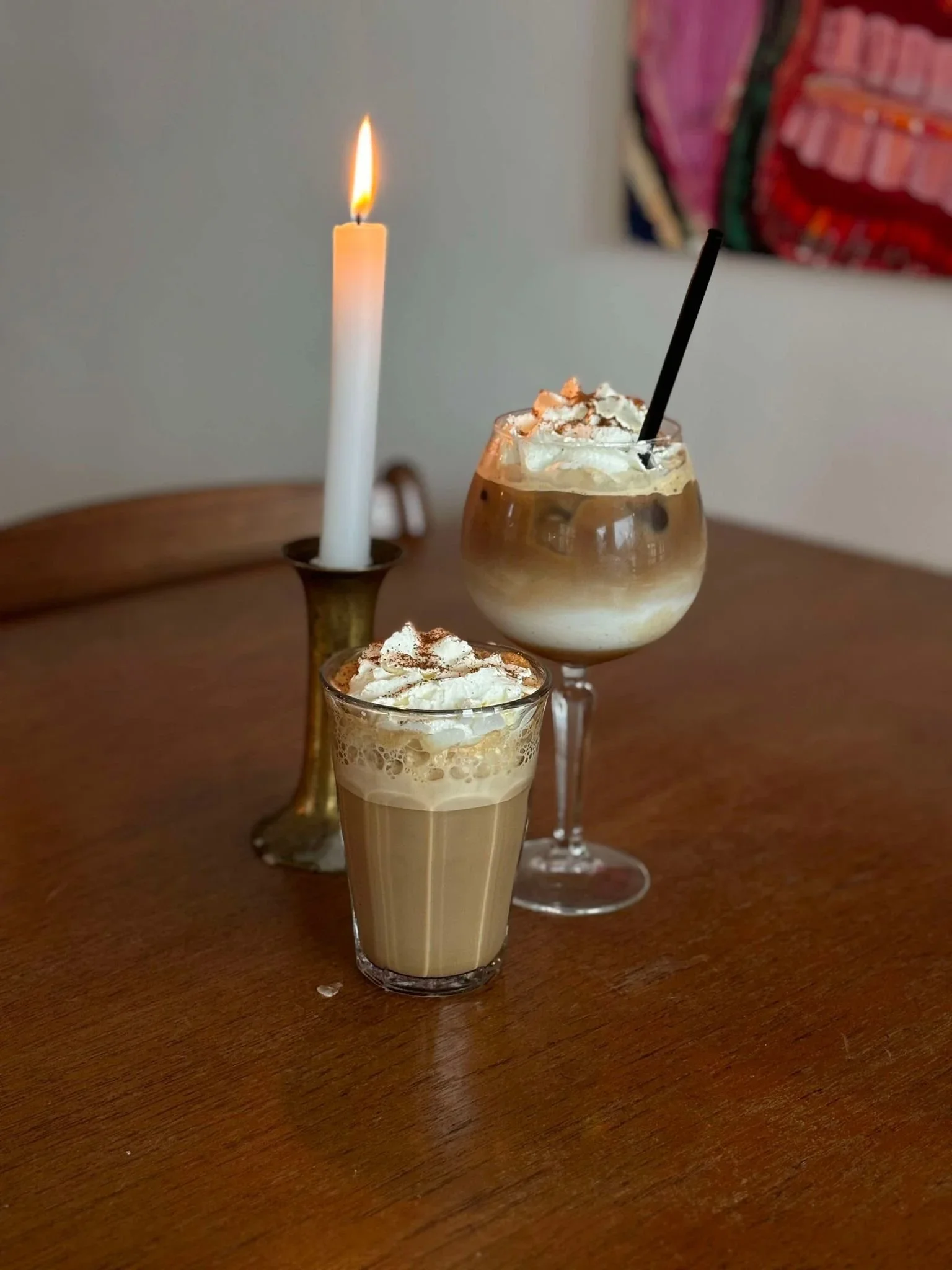 Tre glas med kaffe og flødeskum, lysende stearinlys på et træbord.