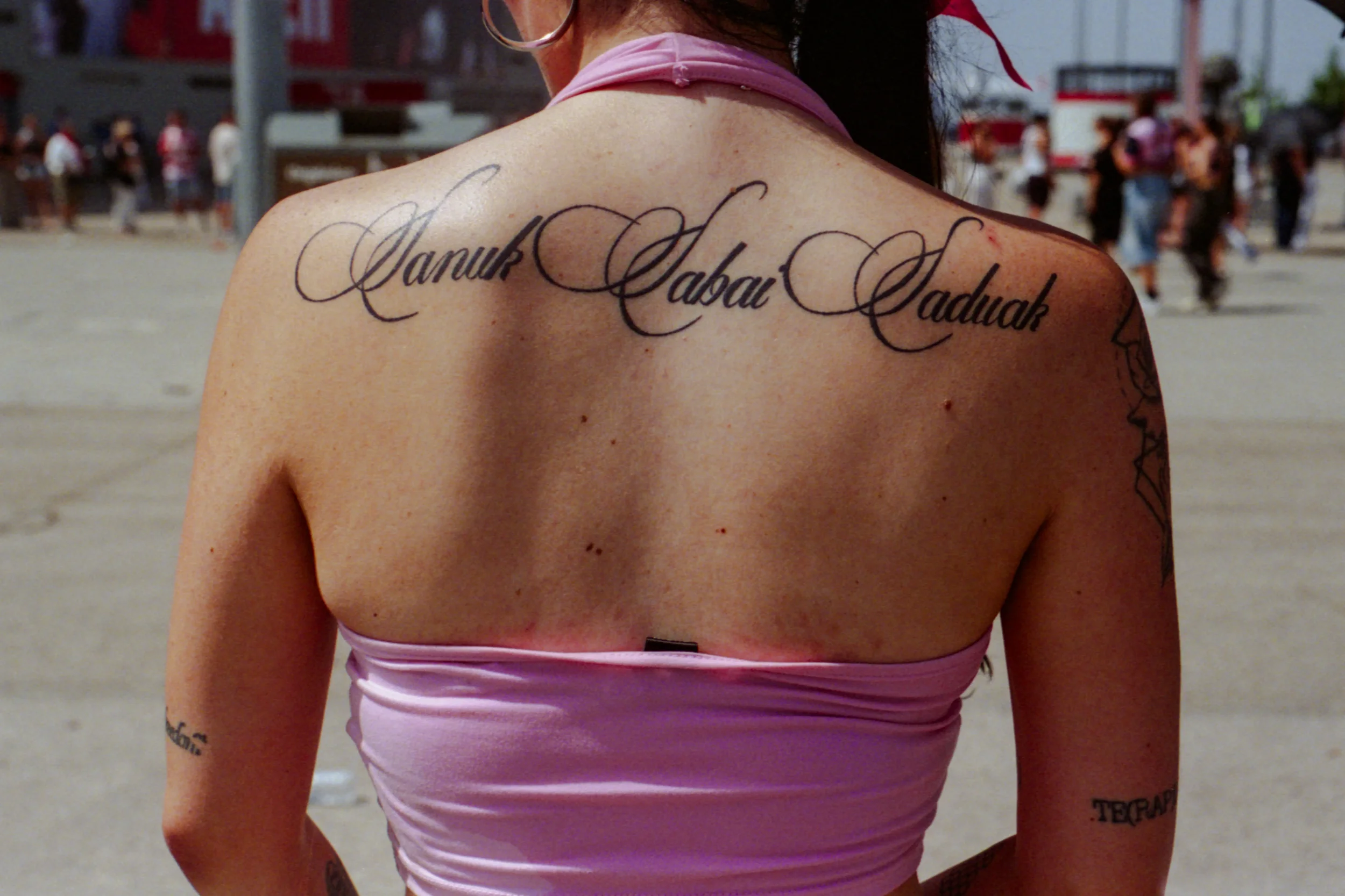 Persona con tatuajes en la espalda y el brazo, lleva puesta una parte superior rosa y gafas.