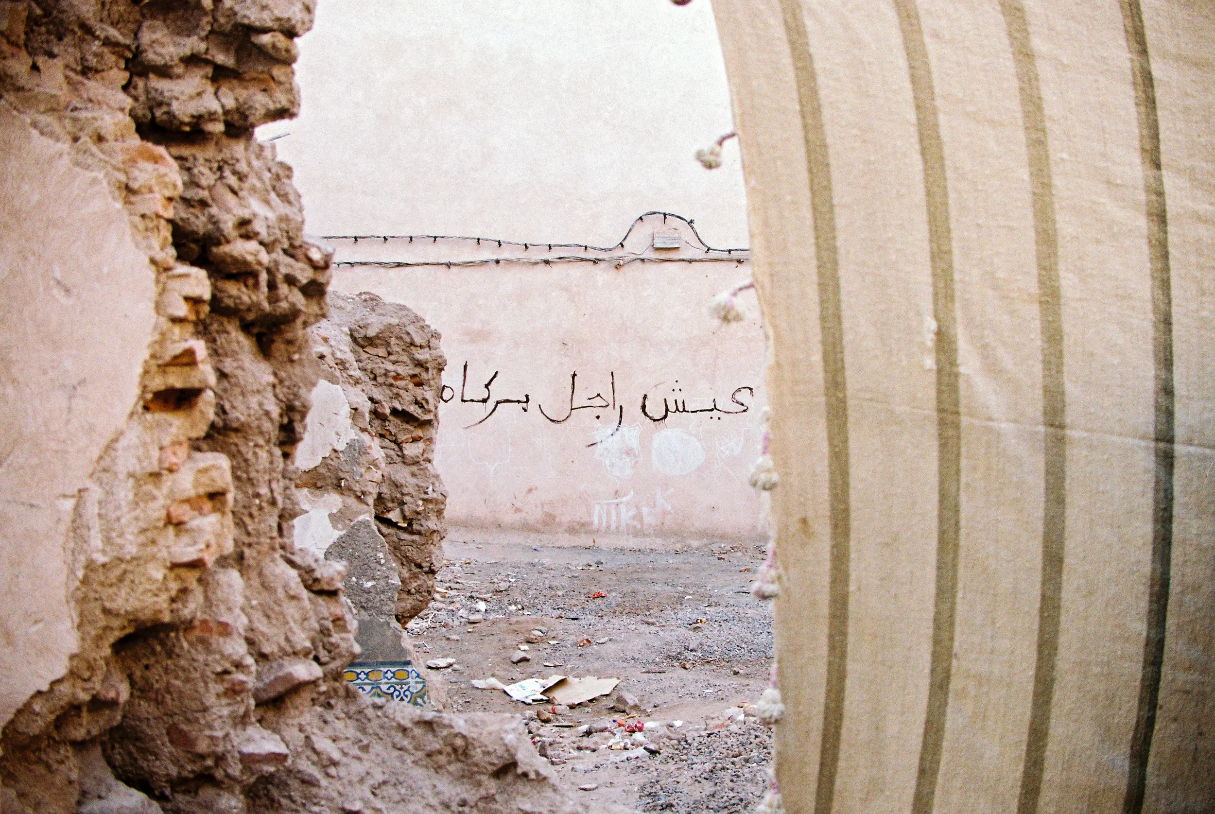 Vista de un callejón entre paredes de ladrillos y concreto, con garabatos en la pared del fondo y basura en el suelo.