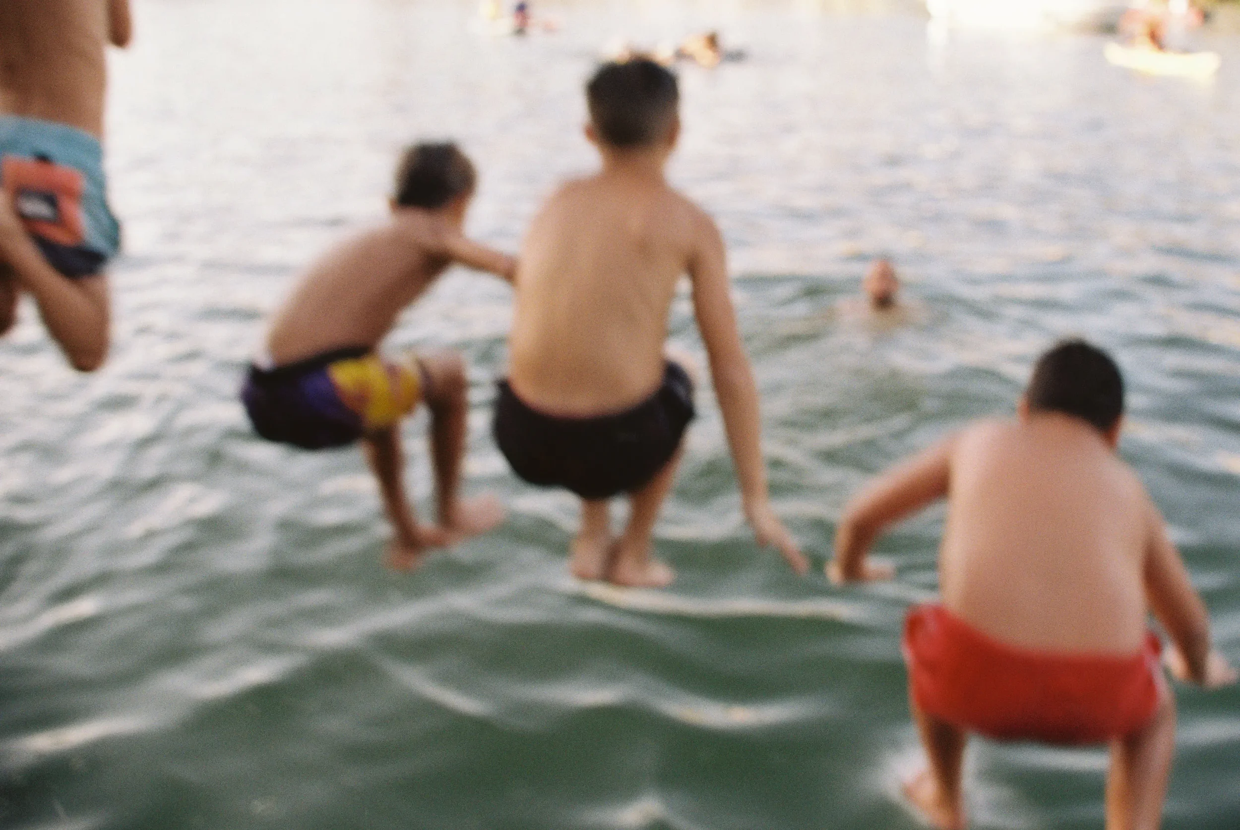 Niños en bañador jugando y metidos en el agua en la playa en un atardecer.