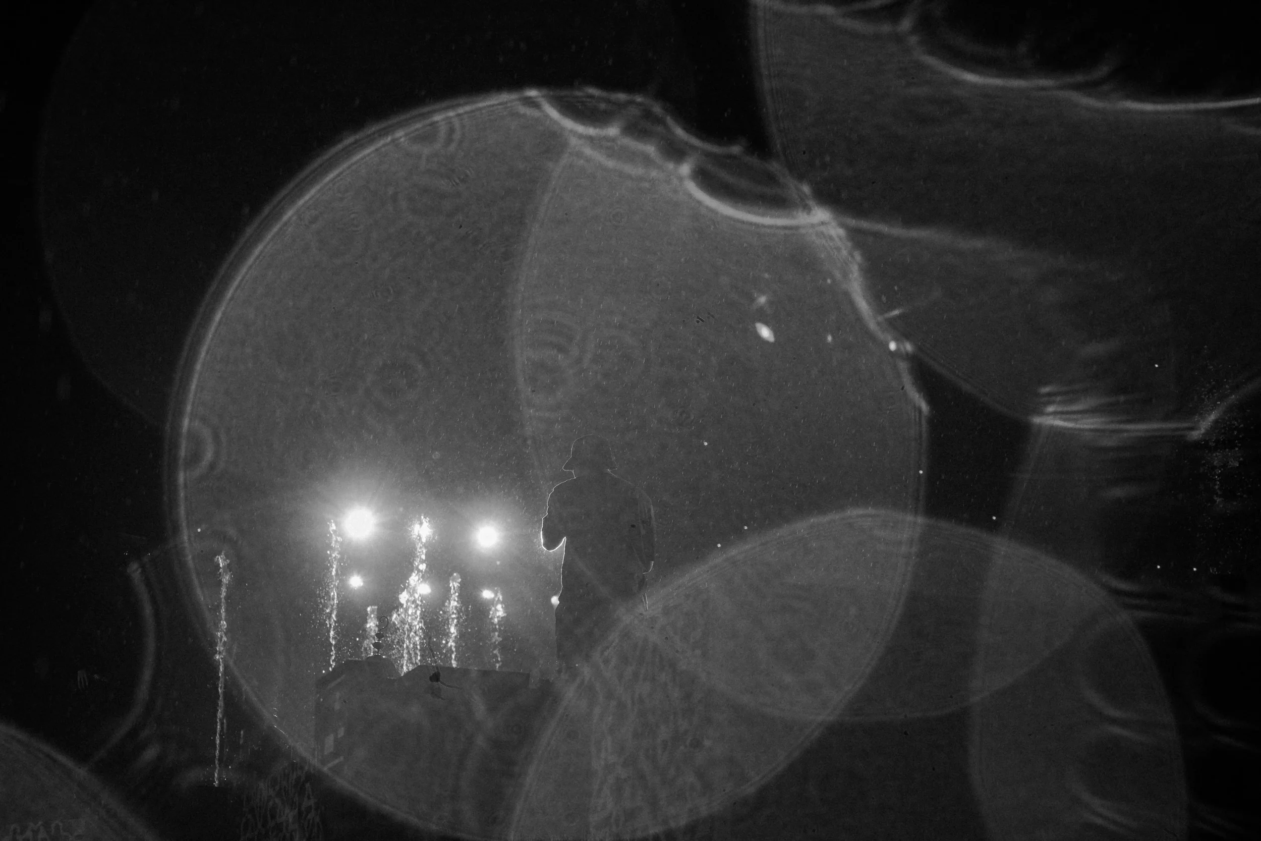 Imagen en blanco y negro que muestra burbujas grandes en un líquido, reflejando luces y una figura humana en el fondo.