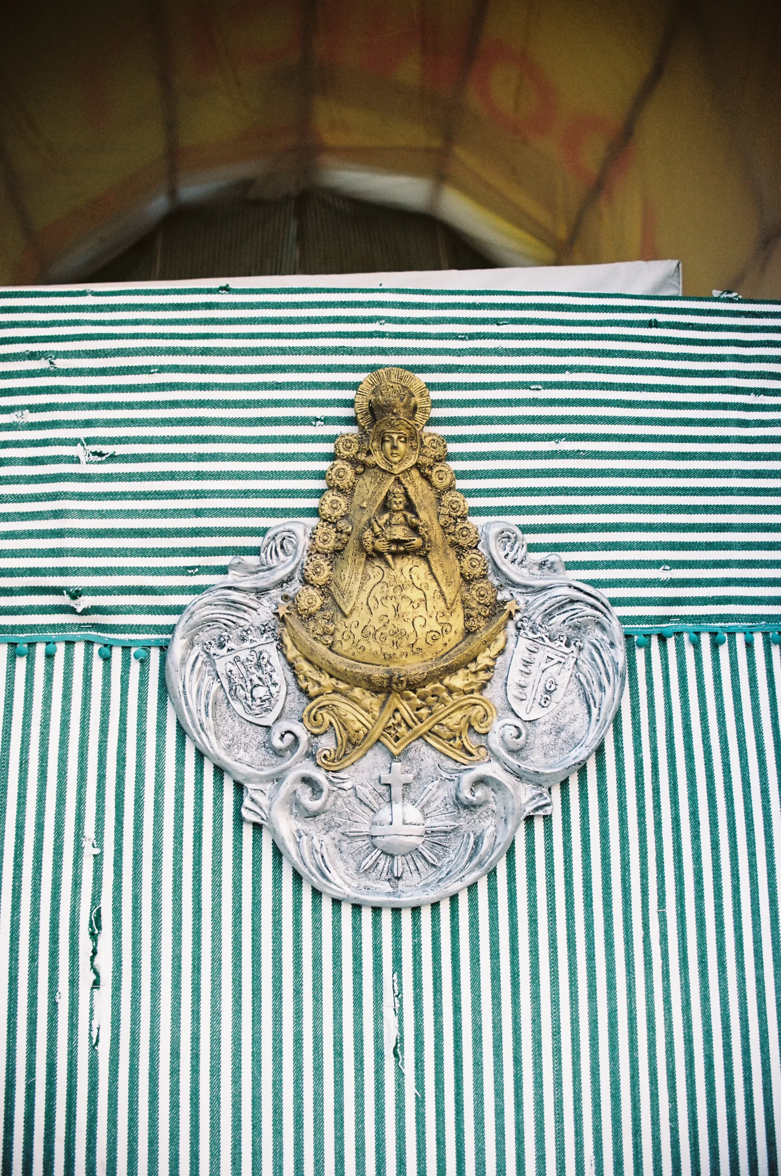 Insignia religiosa en metal dorado y plateado sobre tela con franjas verdes y blancas, en un altar o espacio sagrado.
