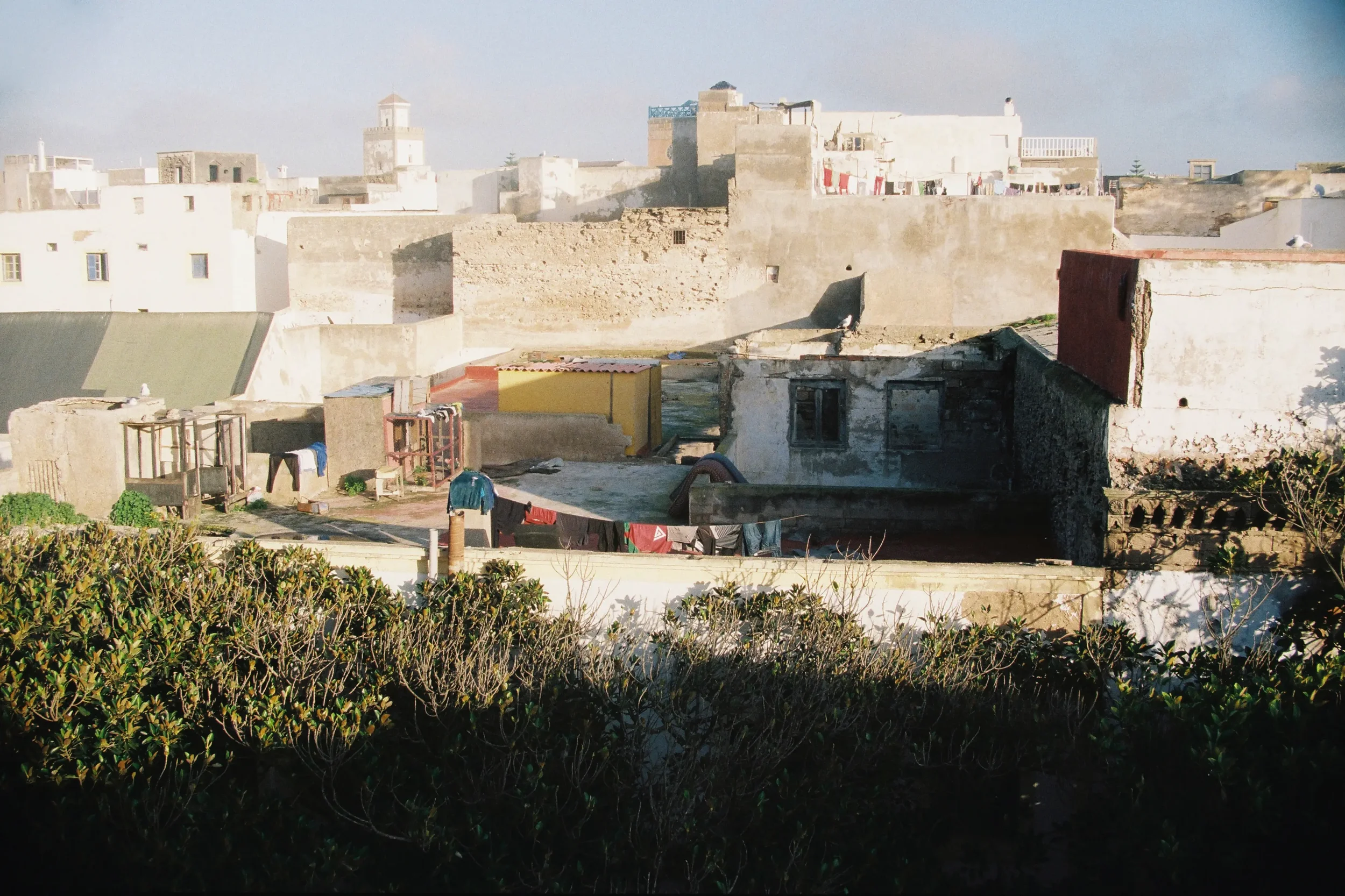 Vista de techos y muros de casas antiguas en un barrio, con ropa colgada en una cuerda y vegetación en primer plano.