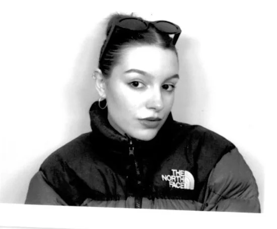 Retrato en blanco y negro de una joven con gafas en la cabeza, en un chaqueta de The North Face, mirando hacia la cámara.