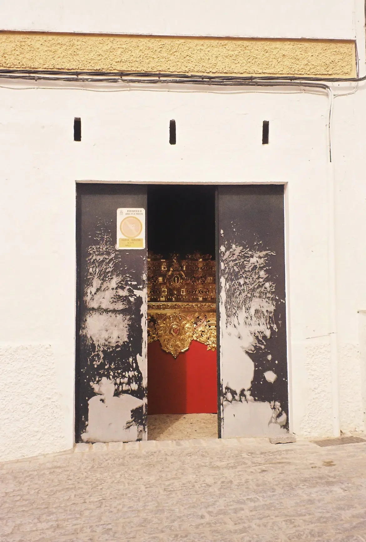 Entrada a una iglesia o templo con puertas abiertas, decoradas con detalles dorados y cortinas rojas en el interior.