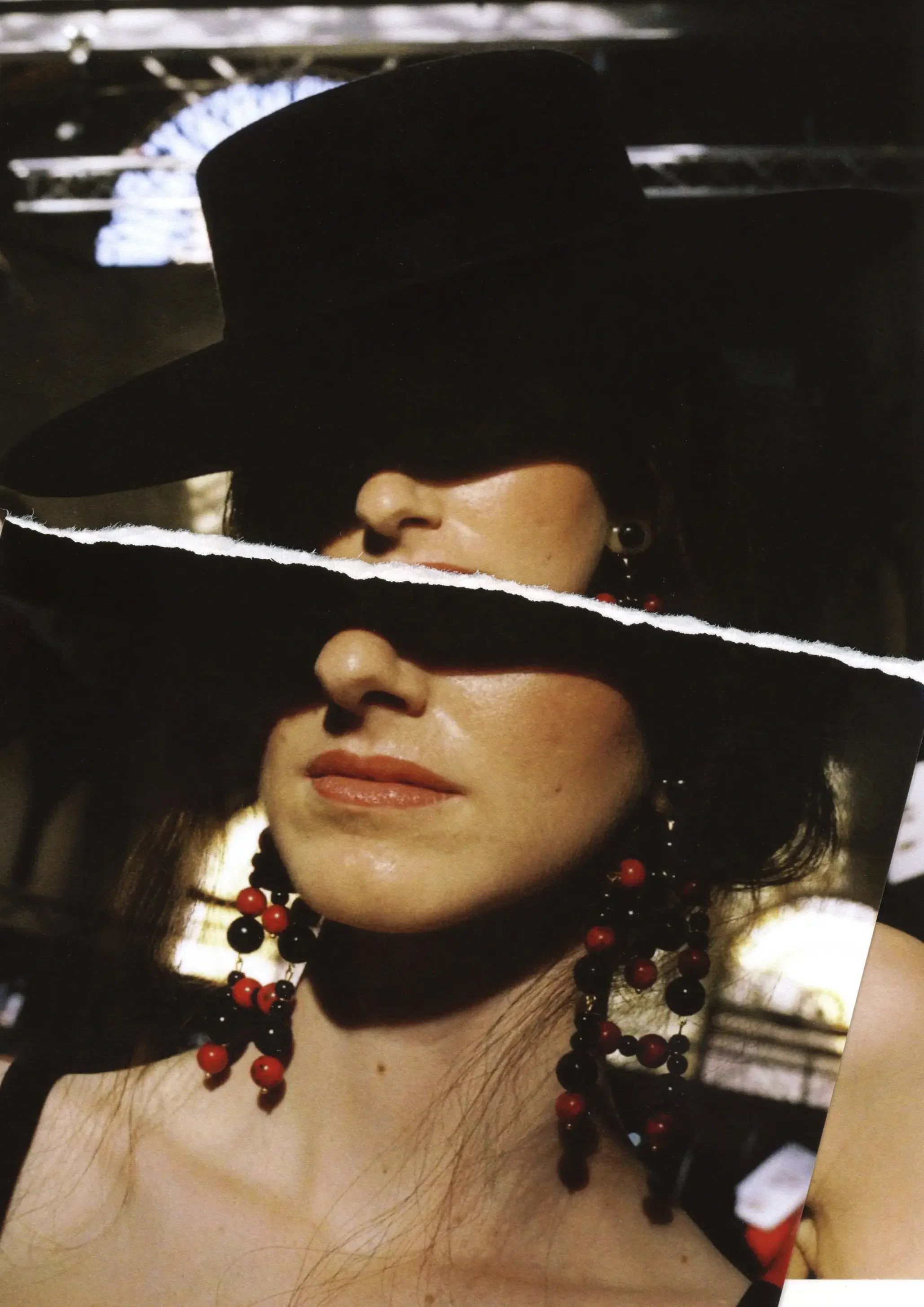 Mujer con sombrero negro grande parcialmente cubriendo su rostro, usando collar de cuentas negras y rojas, con sonrisa suave, en un entorno con luz suave.