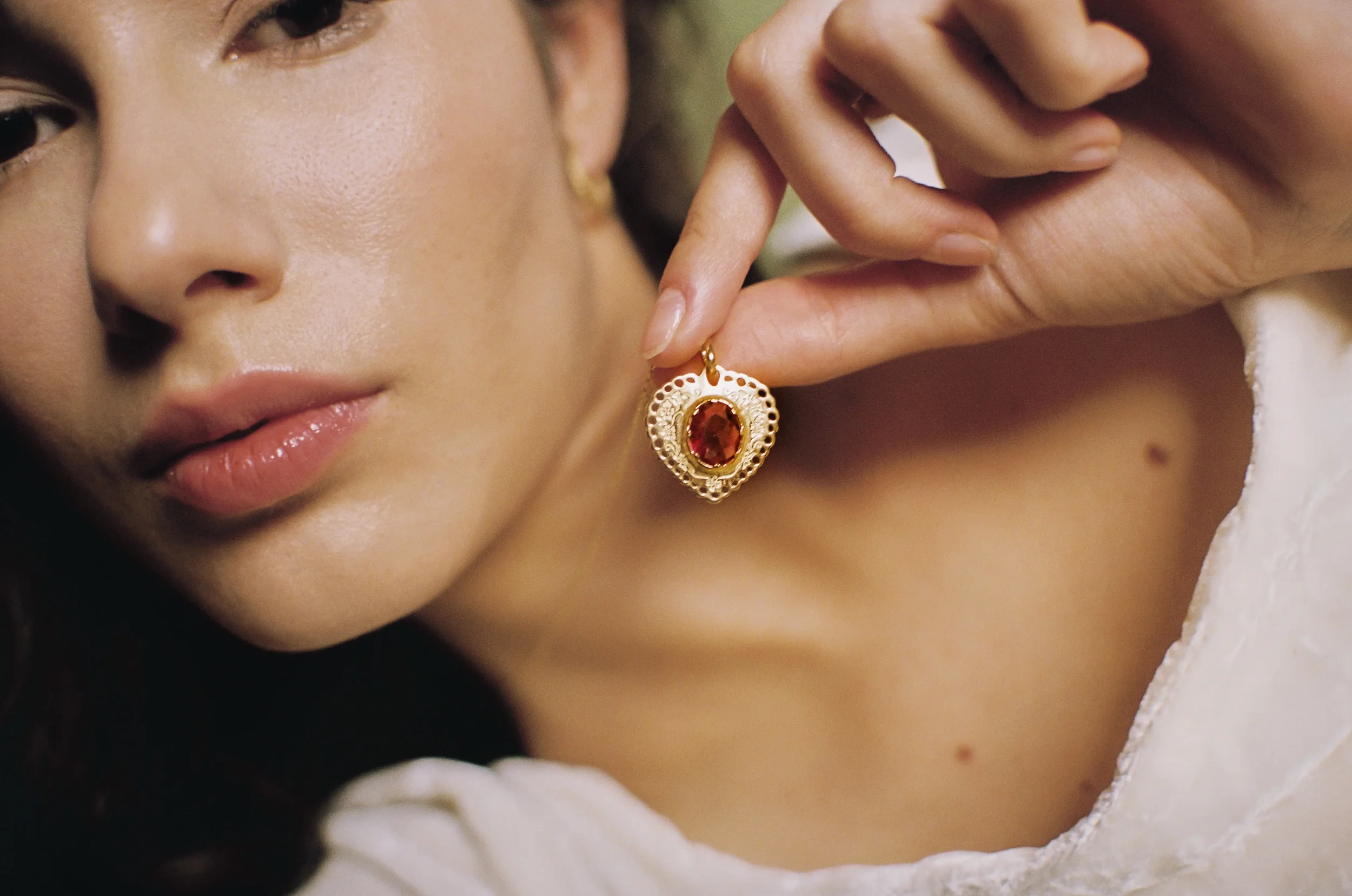 Primer plano del rostro de una mujer con una oreja adornada con un pendiente dorado con piedra roja, tocando su zapato con su dedo índice.