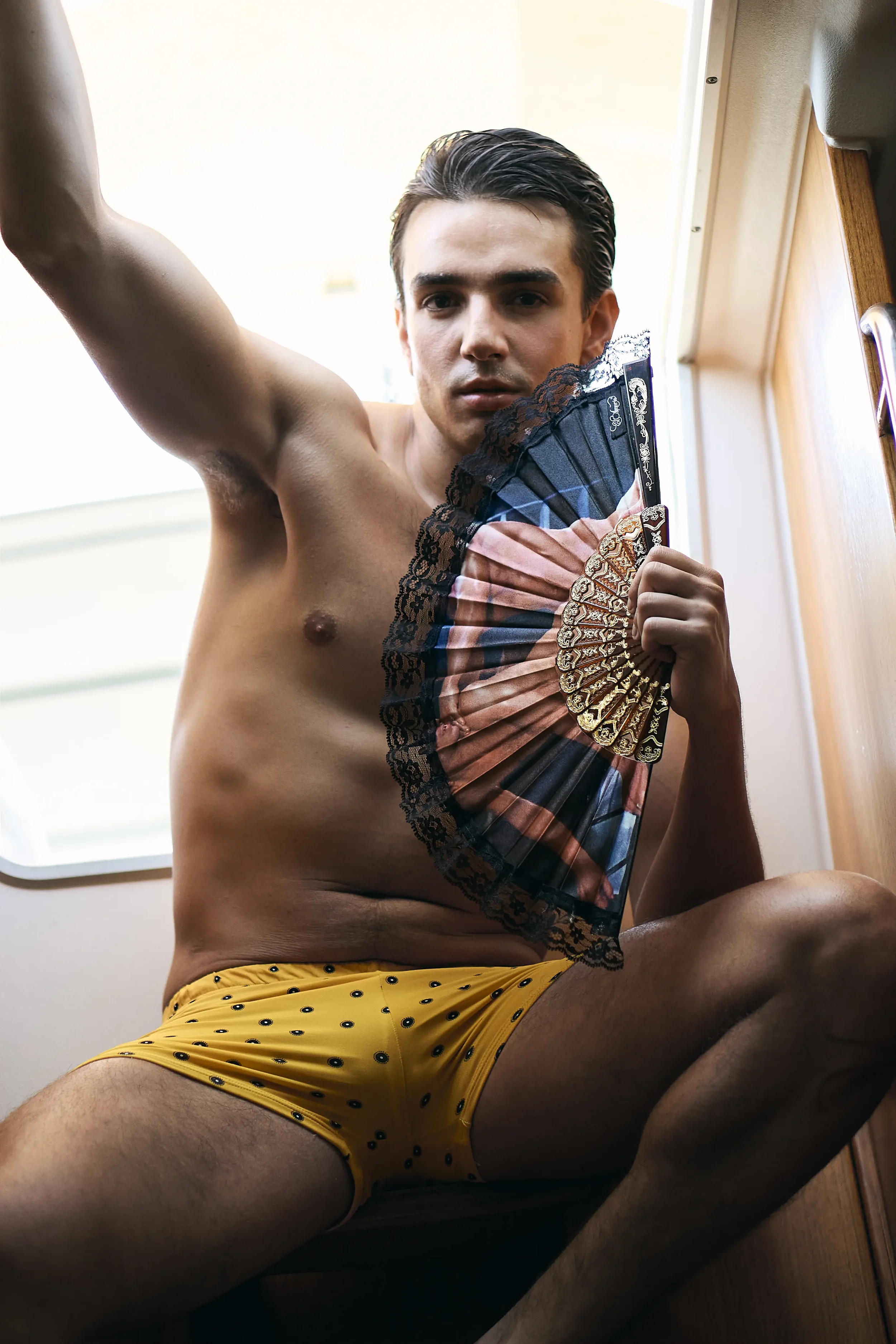 Joven sosteniendo un abanico con pantalones cortos amarillos con puntos negros, en un espacio interior con luz natural.