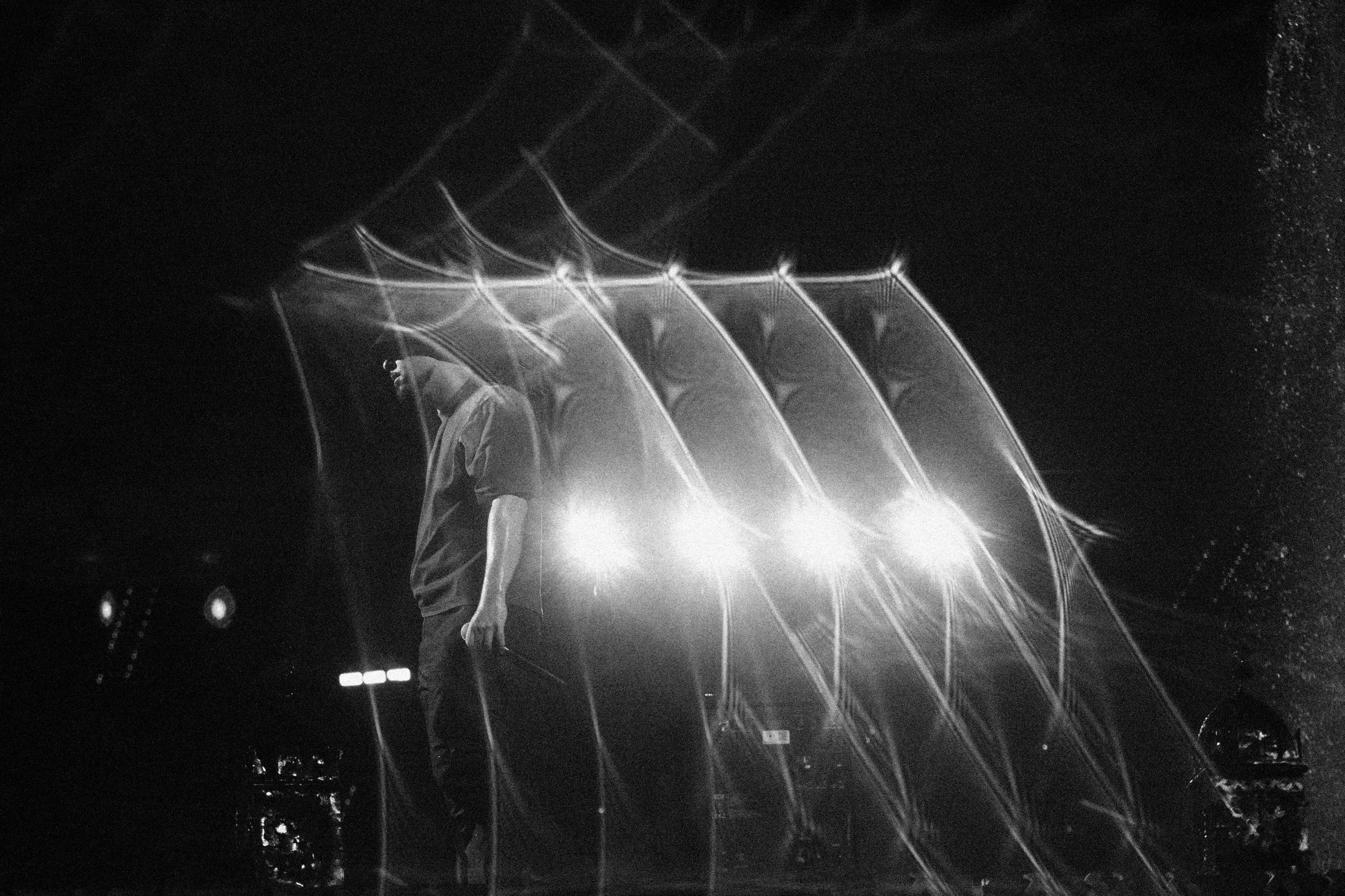 Una persona caminando bajo un arco de luces en un entorno oscuro, con destellos y efectos de iluminación que crean un ambiente futurista y misterioso.