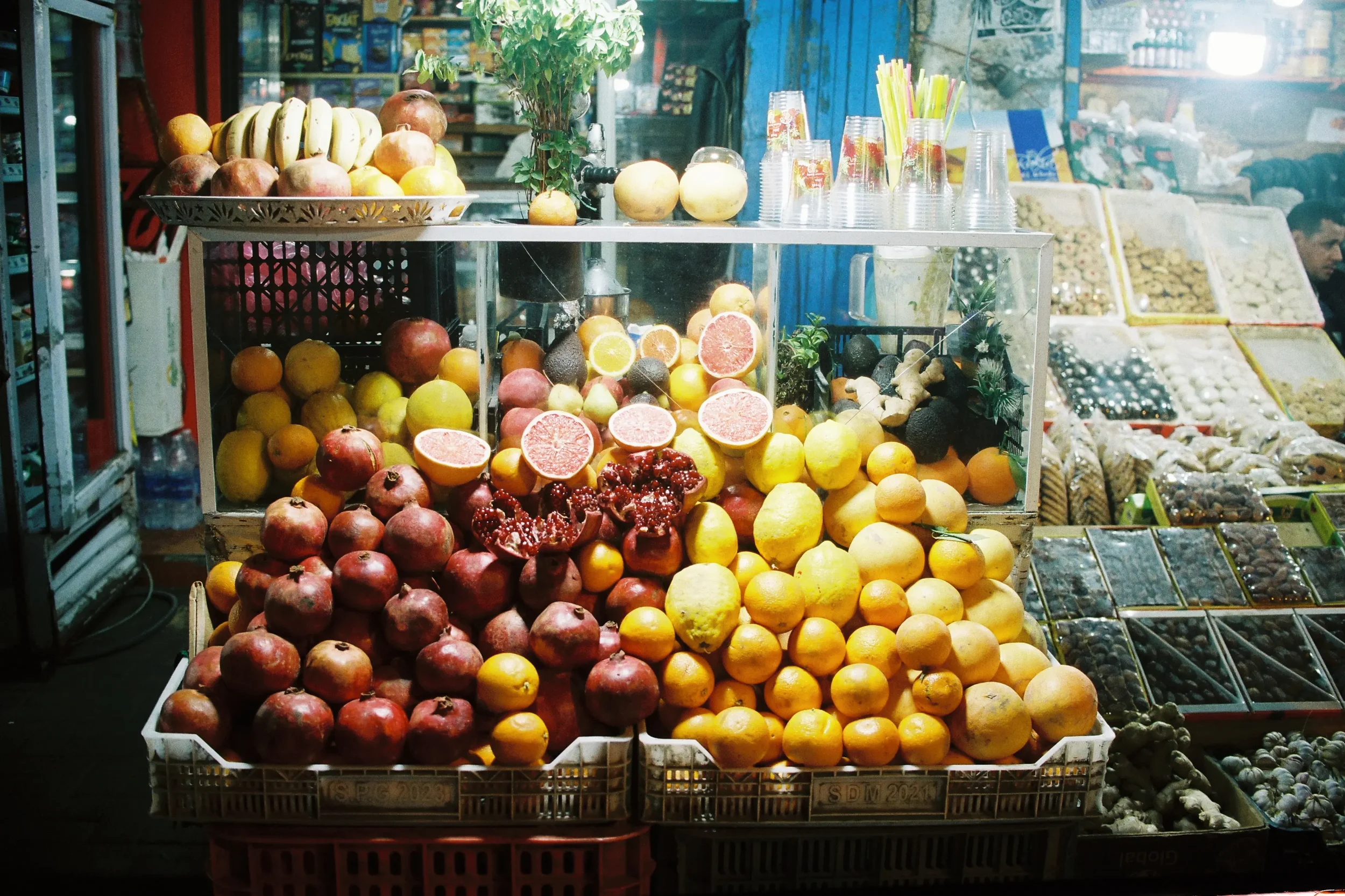 Puesto de frutas con variedad de frutas, incluyendo granadas, limones, naranjas, aguacates, y otros productos en un mercado al aire libre.