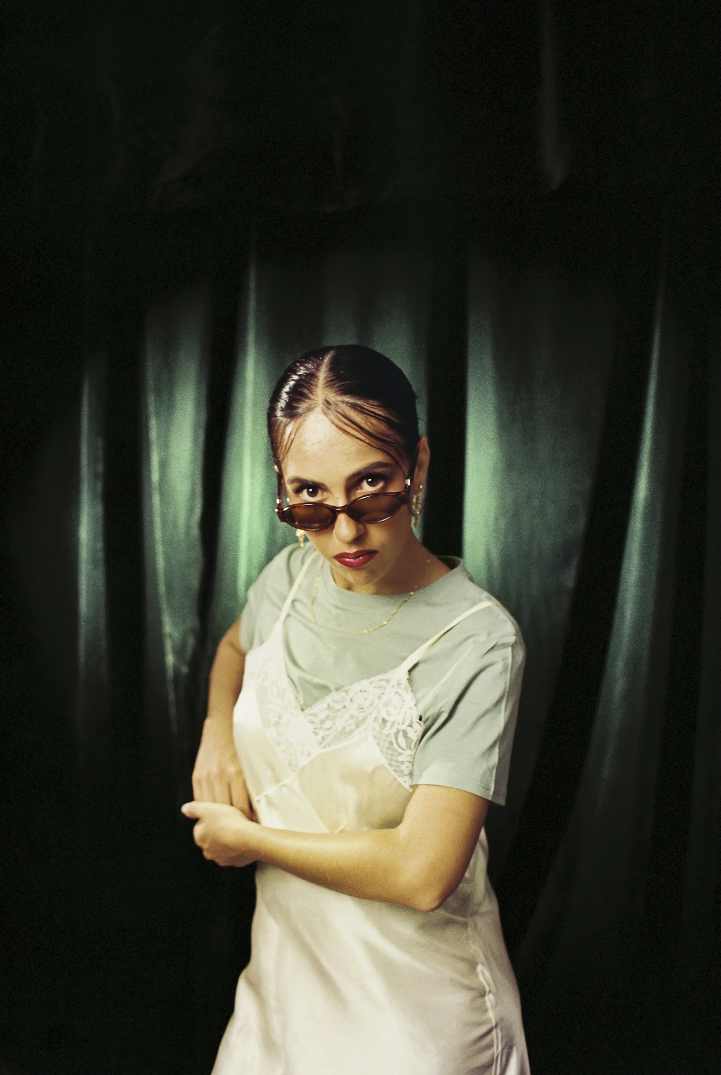 Retrato de una mujer con gafas de sol, peinado recogido y expresión seria, con fondo verde y negro.