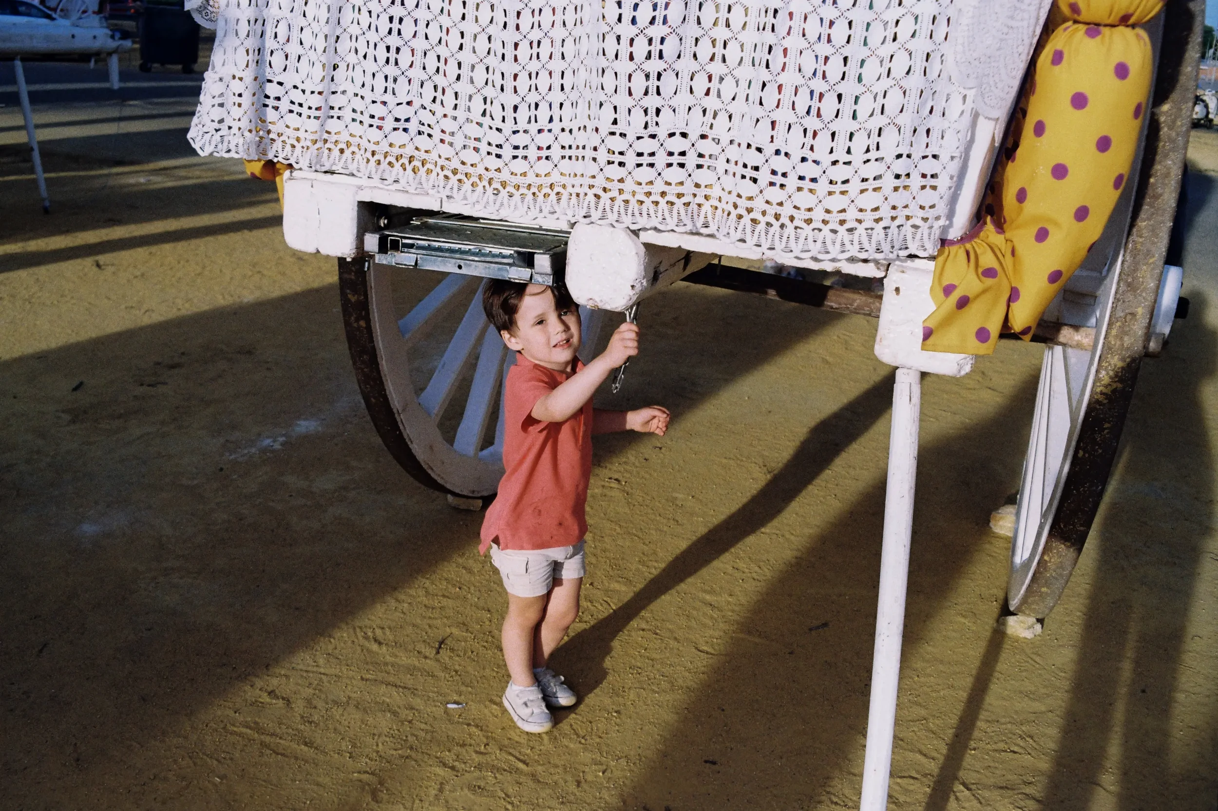 Niño pequeño con camiseta naranja y pantalones beige sosteniendo una llave debajo de una estructura de feria con cortina blanca y decoraciones de tela amarilla con puntos morados.