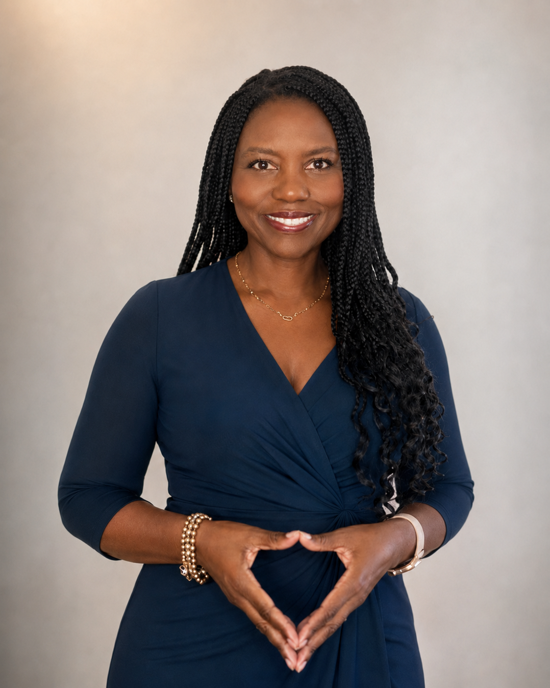 A woman with long braided black hair wearing a navy blue dress, smiling with a neutral background.