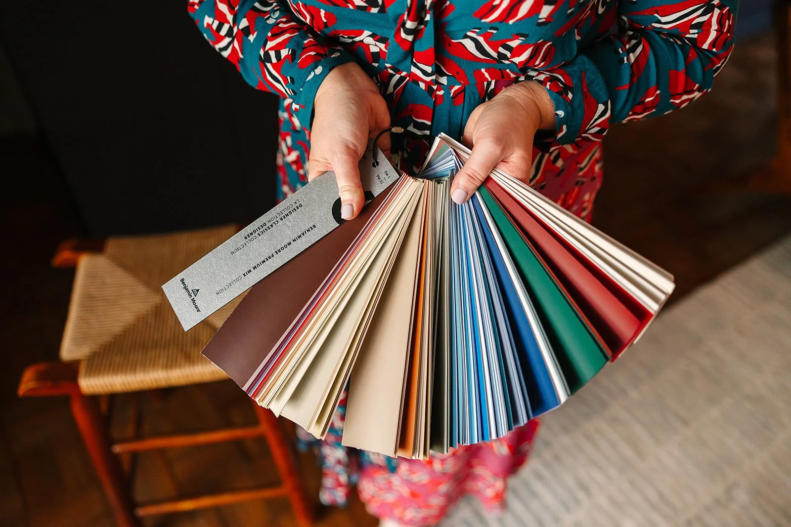 Person holding a color sample fan deck, showcasing various paint color swatches in a home improvement store or showroom.