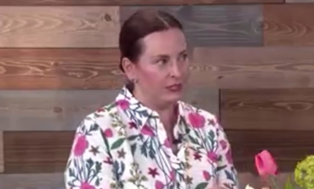Woman wearing a floral shirt sitting in front of a wooden wall.