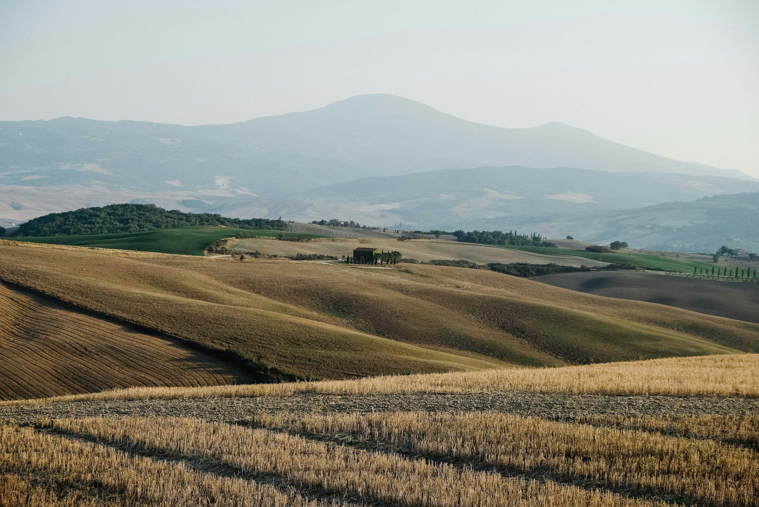 Photograph of rolling hills and farmland with a mountain in the background under a gray sky.