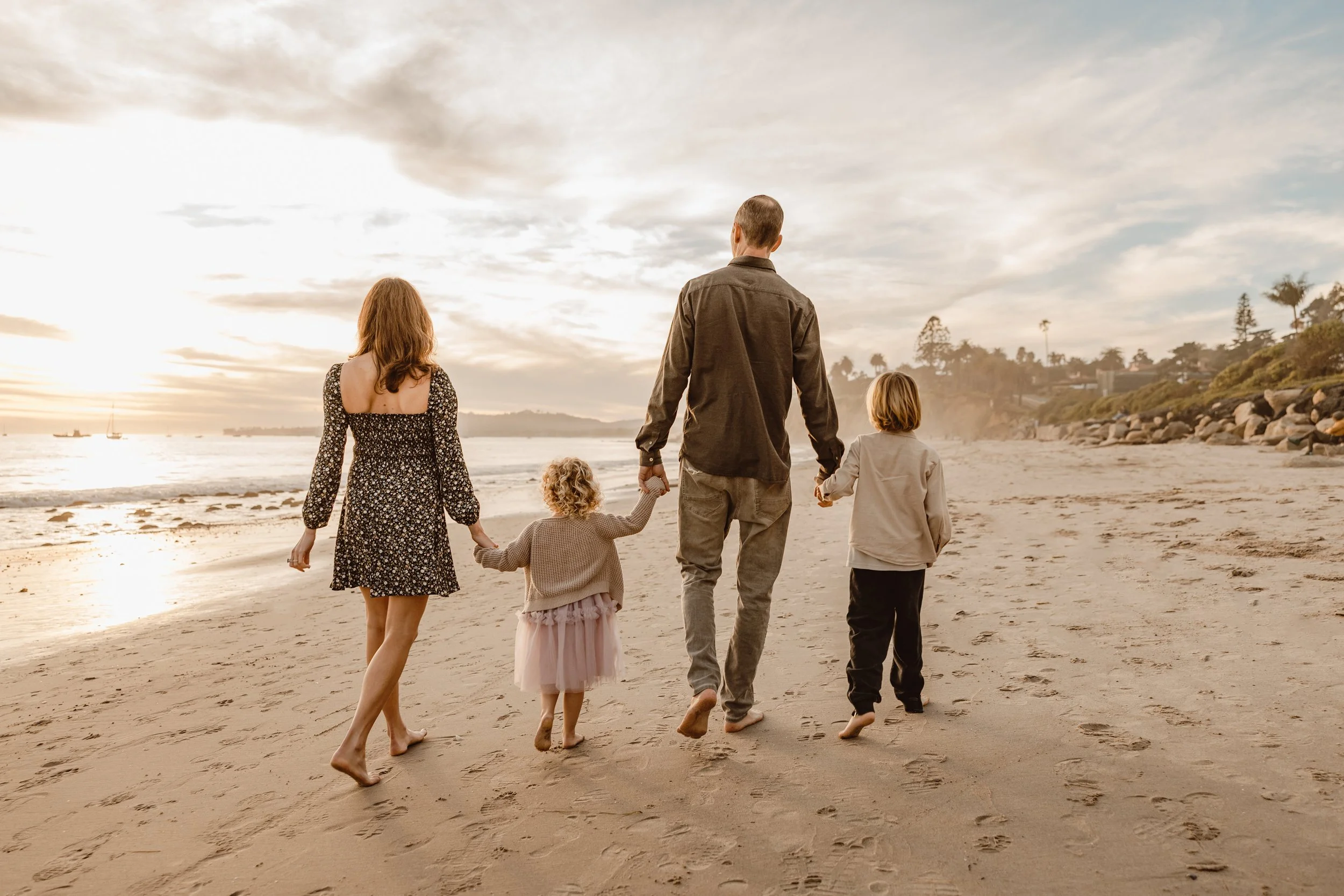 Family walking on the beach holding hands with the sunset in the background.