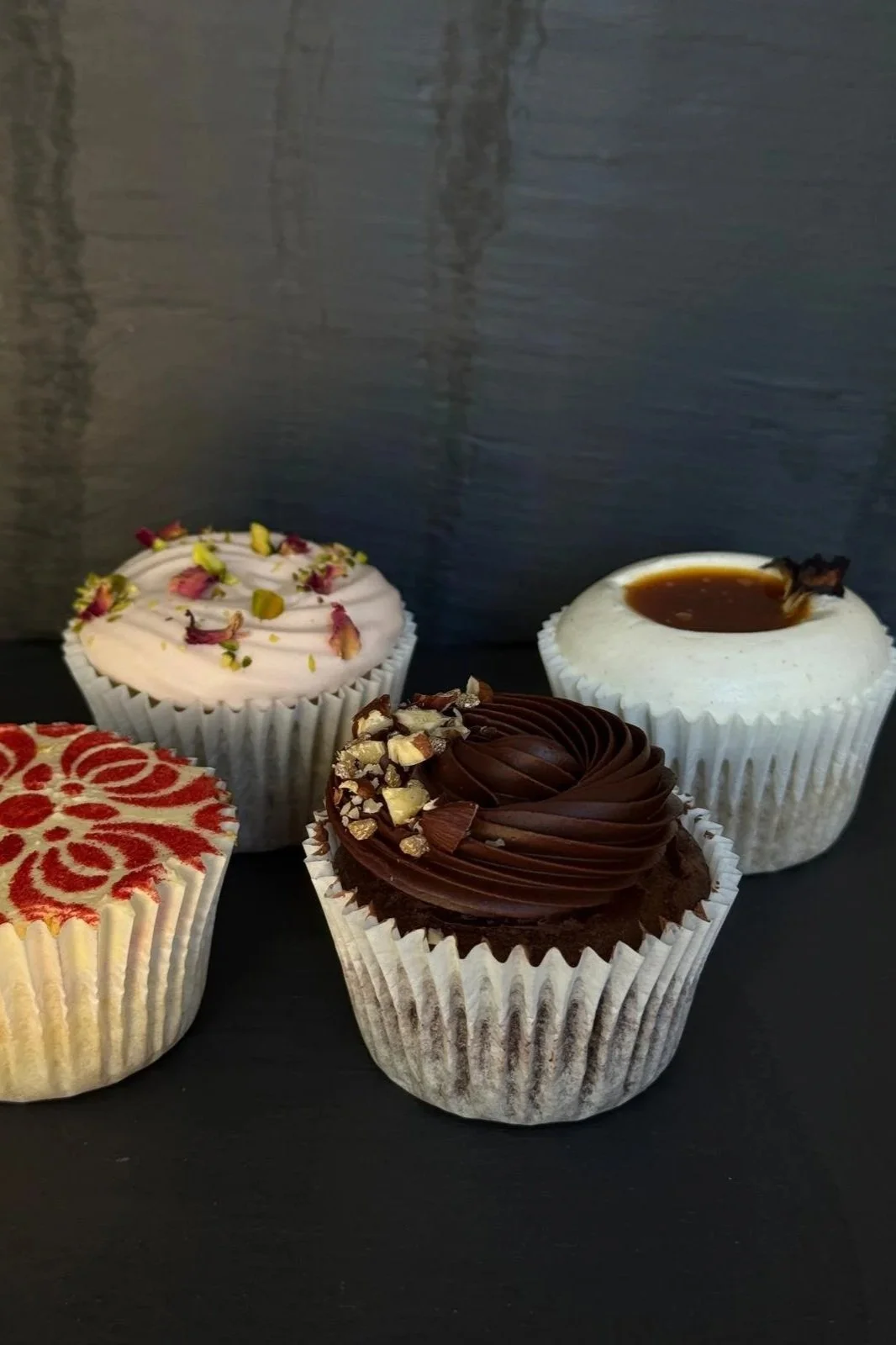 Four decorated cupcakes on a black surface against a dark grey background.