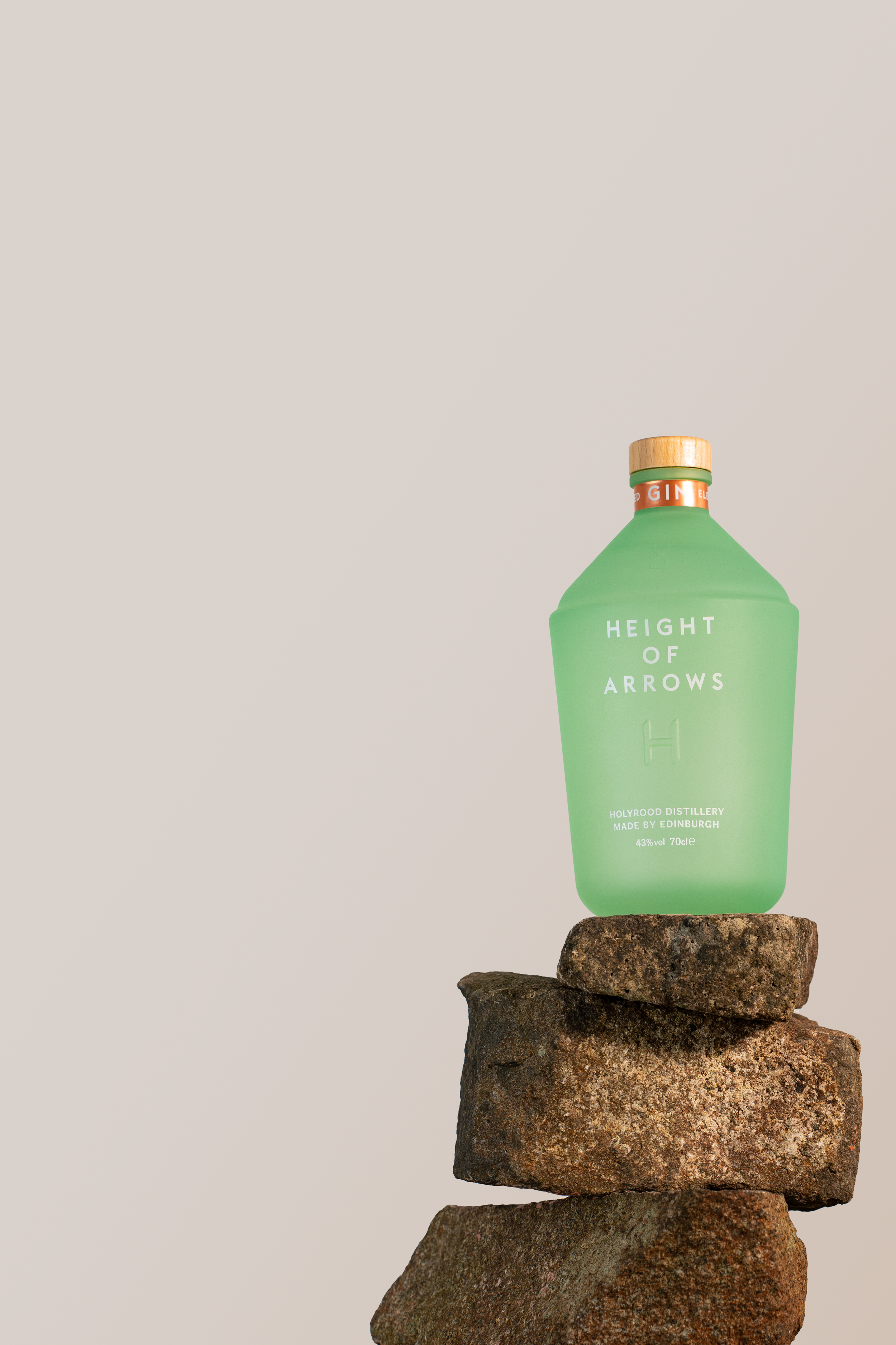 A green bottle of height of arrows whiskey placed on top of stacked rocks against a plain, light background.