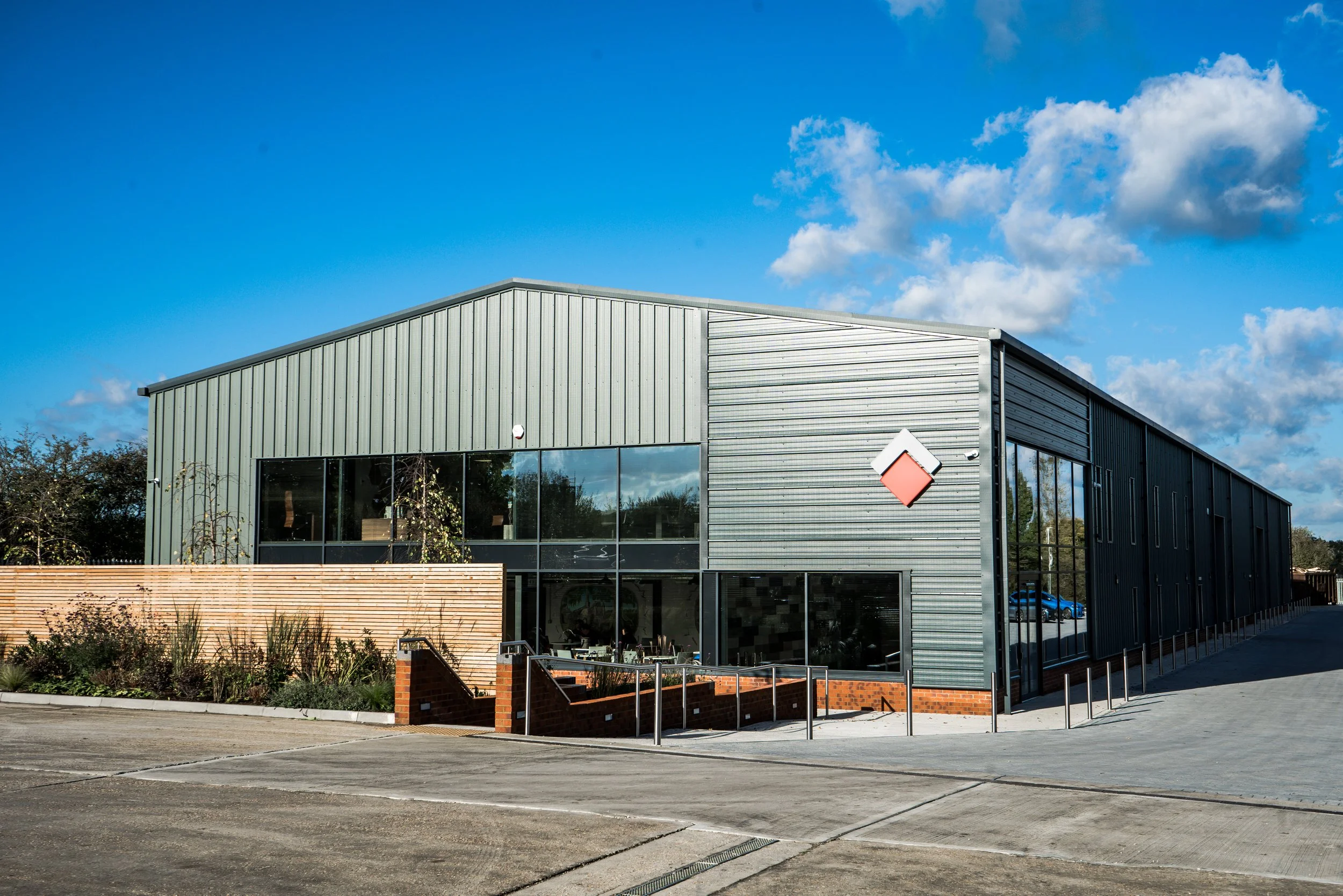 Modern industrial building with metal siding under a blue sky with scattered clouds, parking lot in foreground.