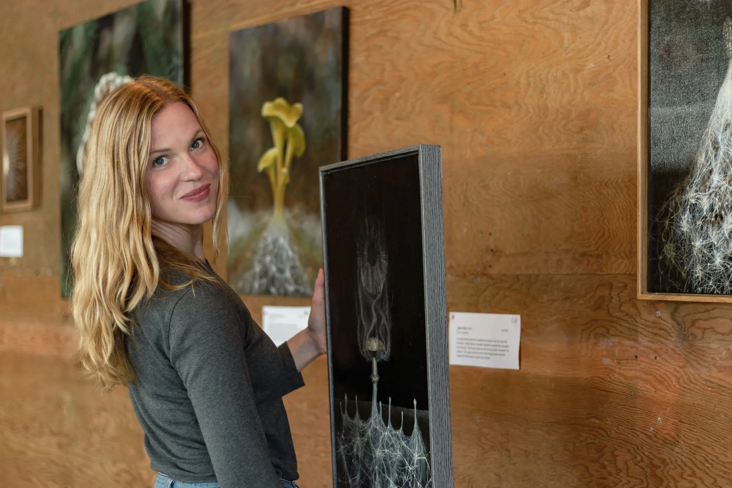 Danielle Masters holding an original oil painting in an art gallery.