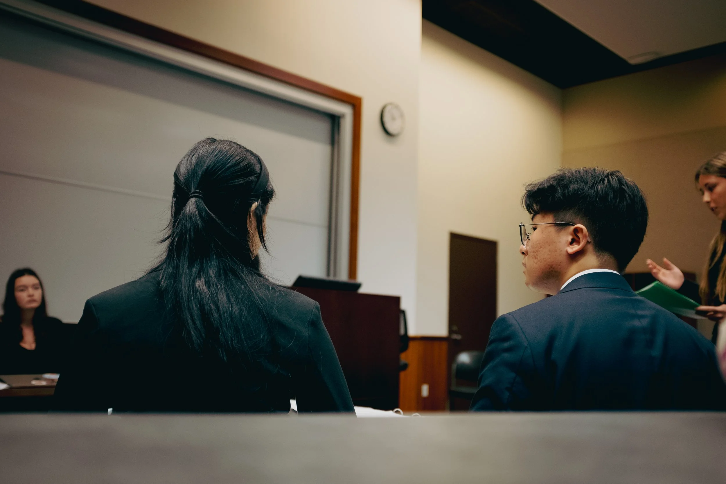 Two high school students sit during a high school mock trial competition, backs facing the camera as they discuss the trial. The Southern California Mock Trial League hosts high school mock trial tournaments across Southern California.
