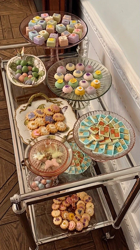 An assortment of colorful desserts including marshmallow treats, chocolate eggs, frosted cookies, and candy-coated chocolates displayed on glass and ceramic trays.