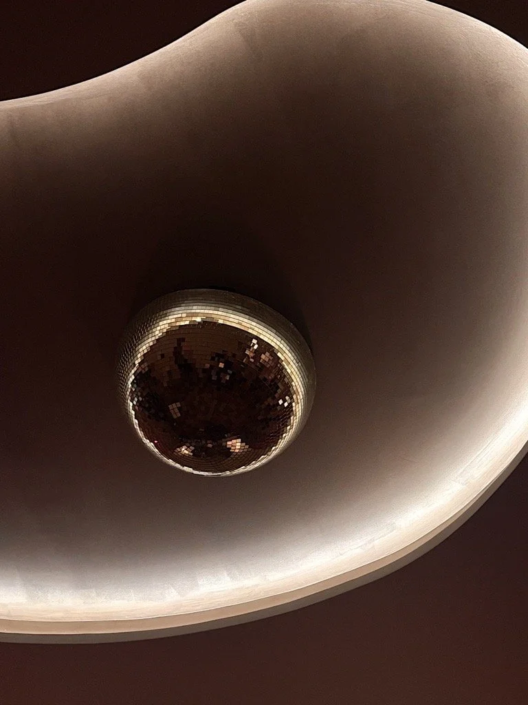 A ceiling with an embedded disco ball surrounded by circular, curved lighting.